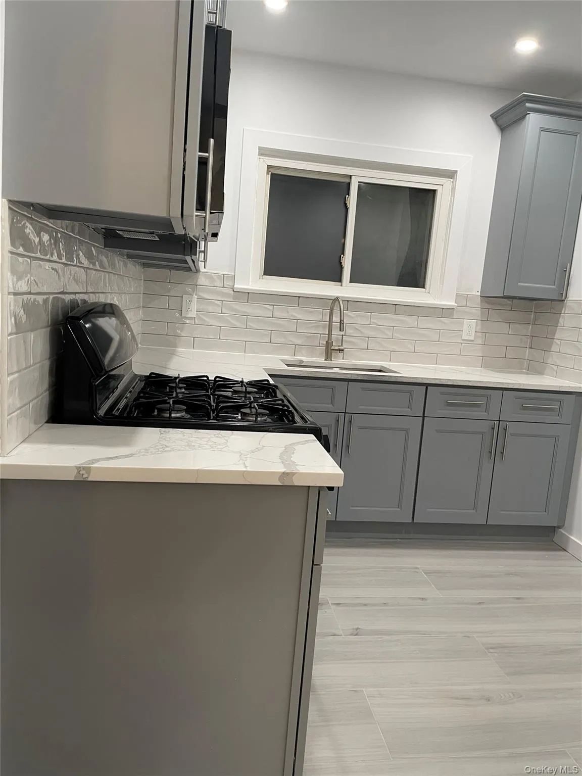 Kitchen with gray cabinets, light stone counters, backsplash, and recessed lighting Kitchen with gray cabinets, light stone counters, backsplash, and recessed lighting