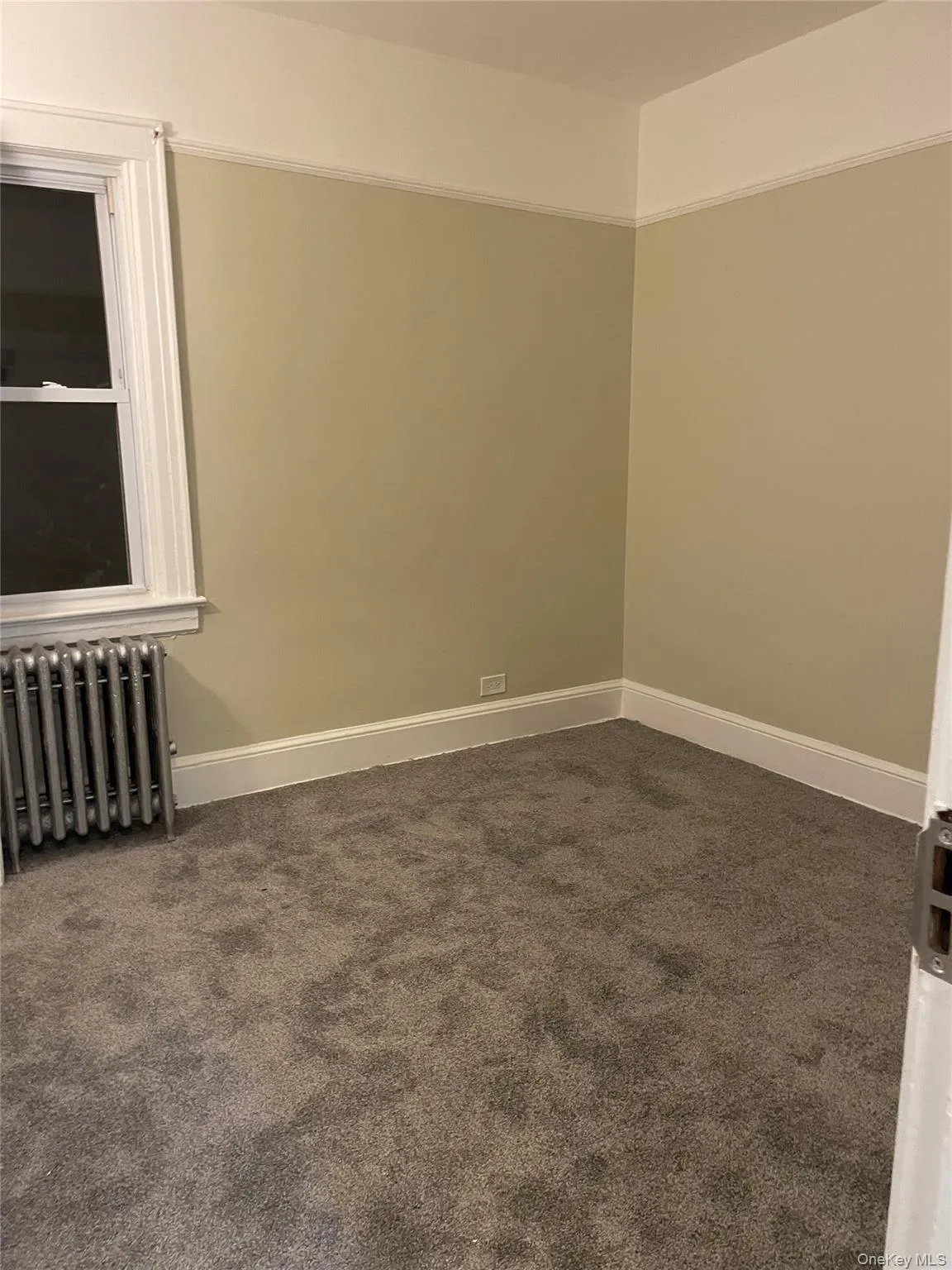 Unfurnished room with radiator heating unit and dark colored carpet Unfurnished room with radiator heating unit and dark colored carpet