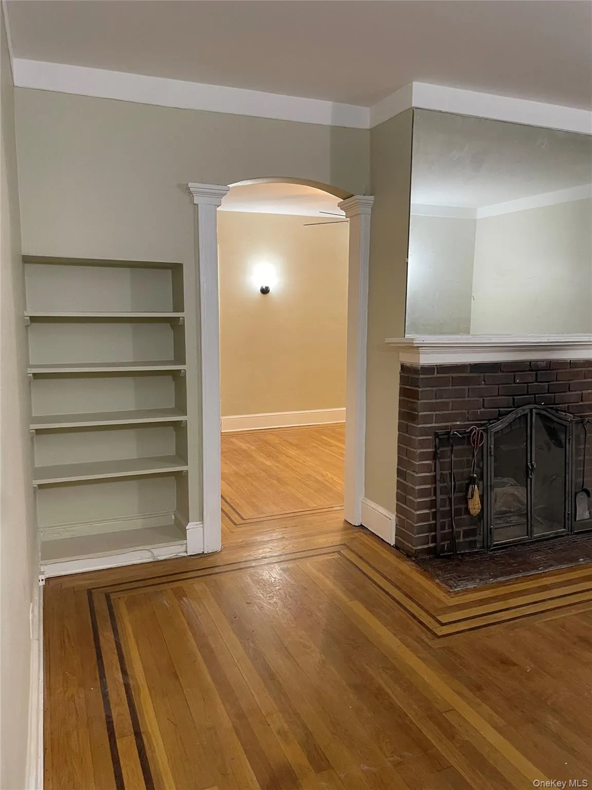 Unfurnished living room featuring arched walkways, a brick fireplace, hardwood / wood-style floors, and ornamental molding Unfurnished living room featuring arched walkways, a brick fireplace, hardwood / wood-style floors, and ornamental molding