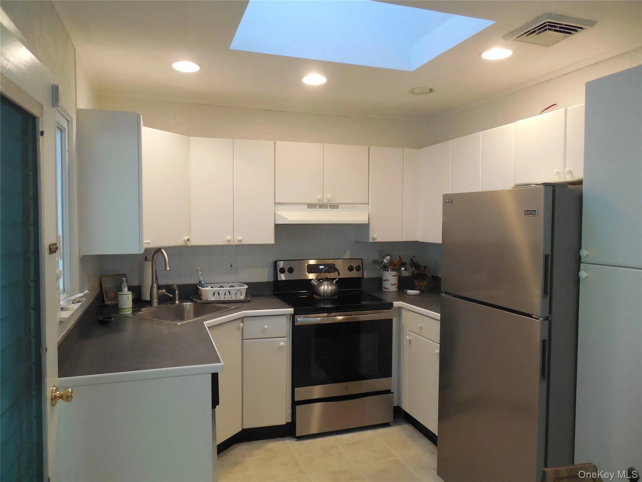 Kitchen with appliances with stainless steel finishes, white cabinets, a skylight, dark countertops, and recessed lighting Kitchen with appliances with stainless steel finishes, white cabinets, a skylight, dark countertops, and recessed lighting
