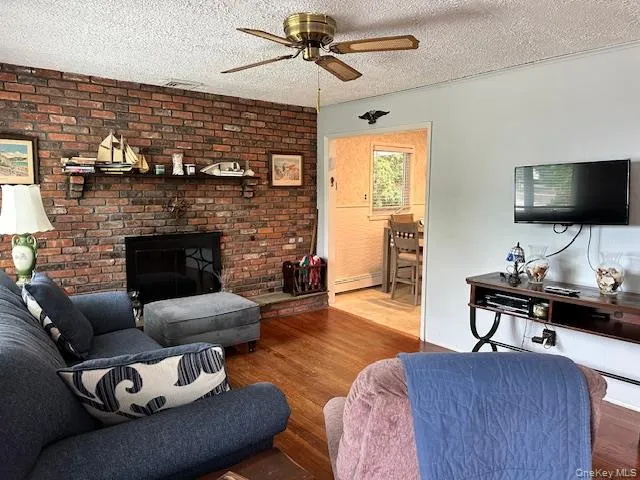 Living area featuring wood finished floors, a fireplace, a textured ceiling, a ceiling fan, and brick wall Living area featuring wood finished floors, a fireplace, a textured ceiling, a ceiling fan, and brick wall