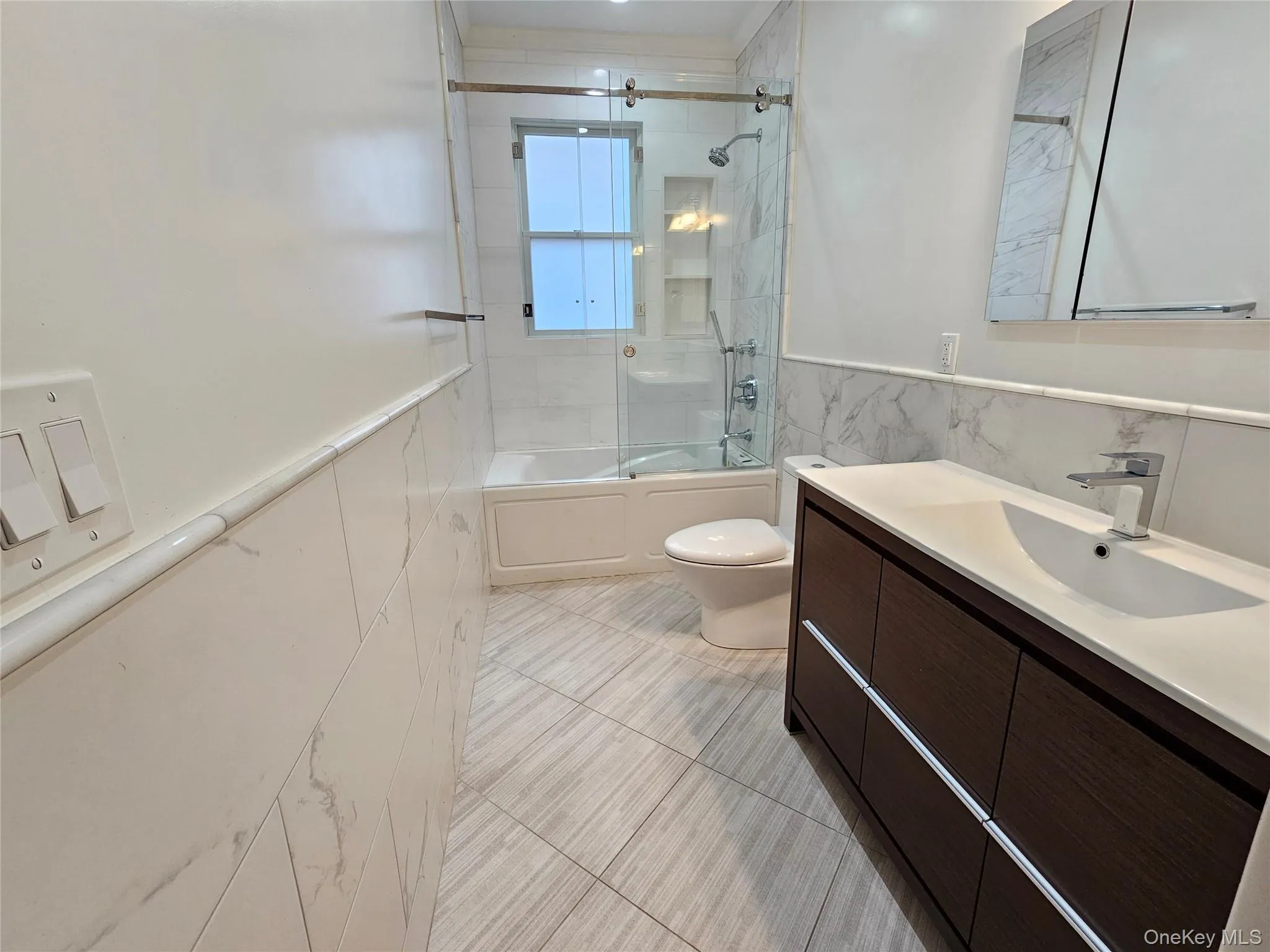 Full bath with a wainscoted wall, enclosed tub / shower combo, vanity, and tile walls Full bath with a wainscoted wall, enclosed tub / shower combo, vanity, and tile walls