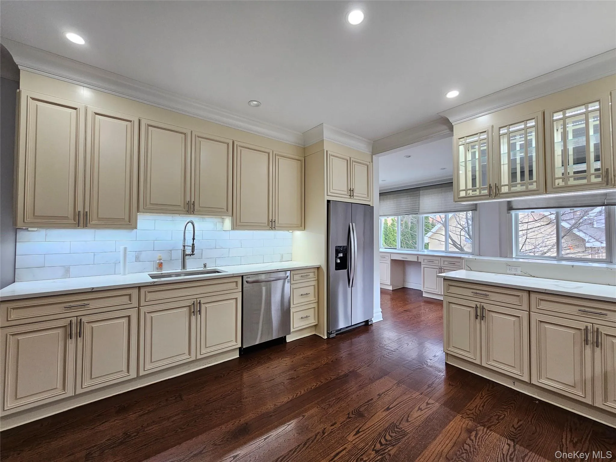 Kitchen featuring cream cabinetry, stainless steel appliances, crown molding, dark wood finished floors, and light stone counters Kitchen featuring cream cabinetry, stainless steel appliances, crown molding, dark wood finished floors, and light stone counters