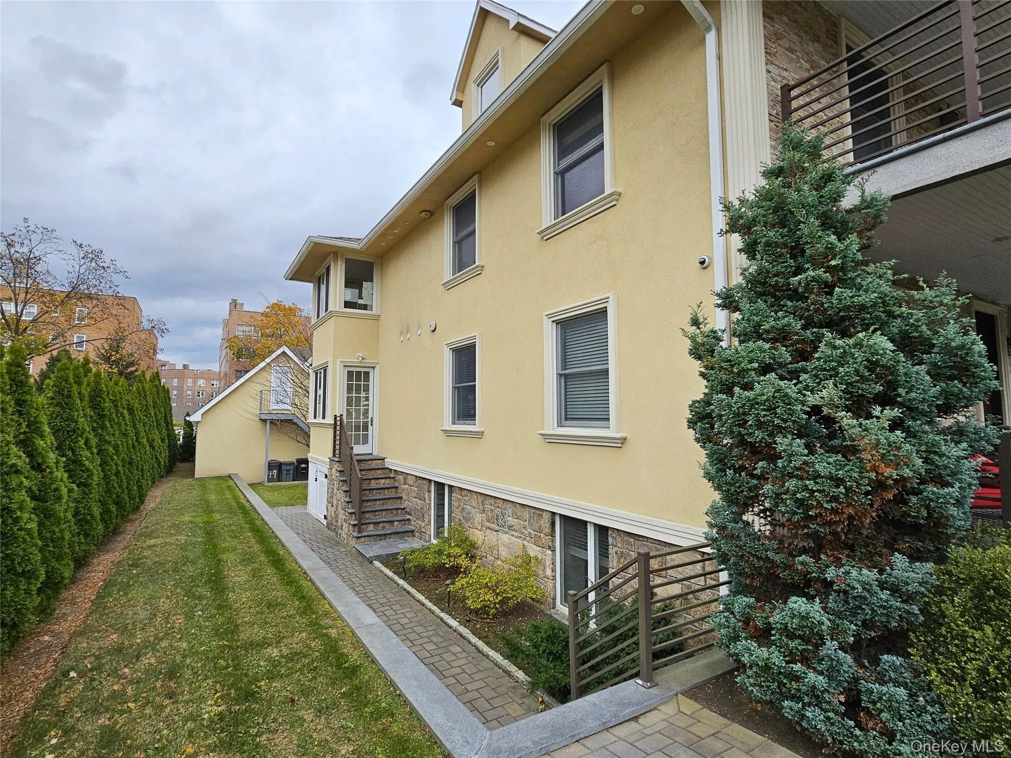 View of property exterior featuring stucco siding, a lawn, stone siding, a balcony, and stairs View of property exterior featuring stucco siding, a lawn, stone siding, a balcony, and stairs