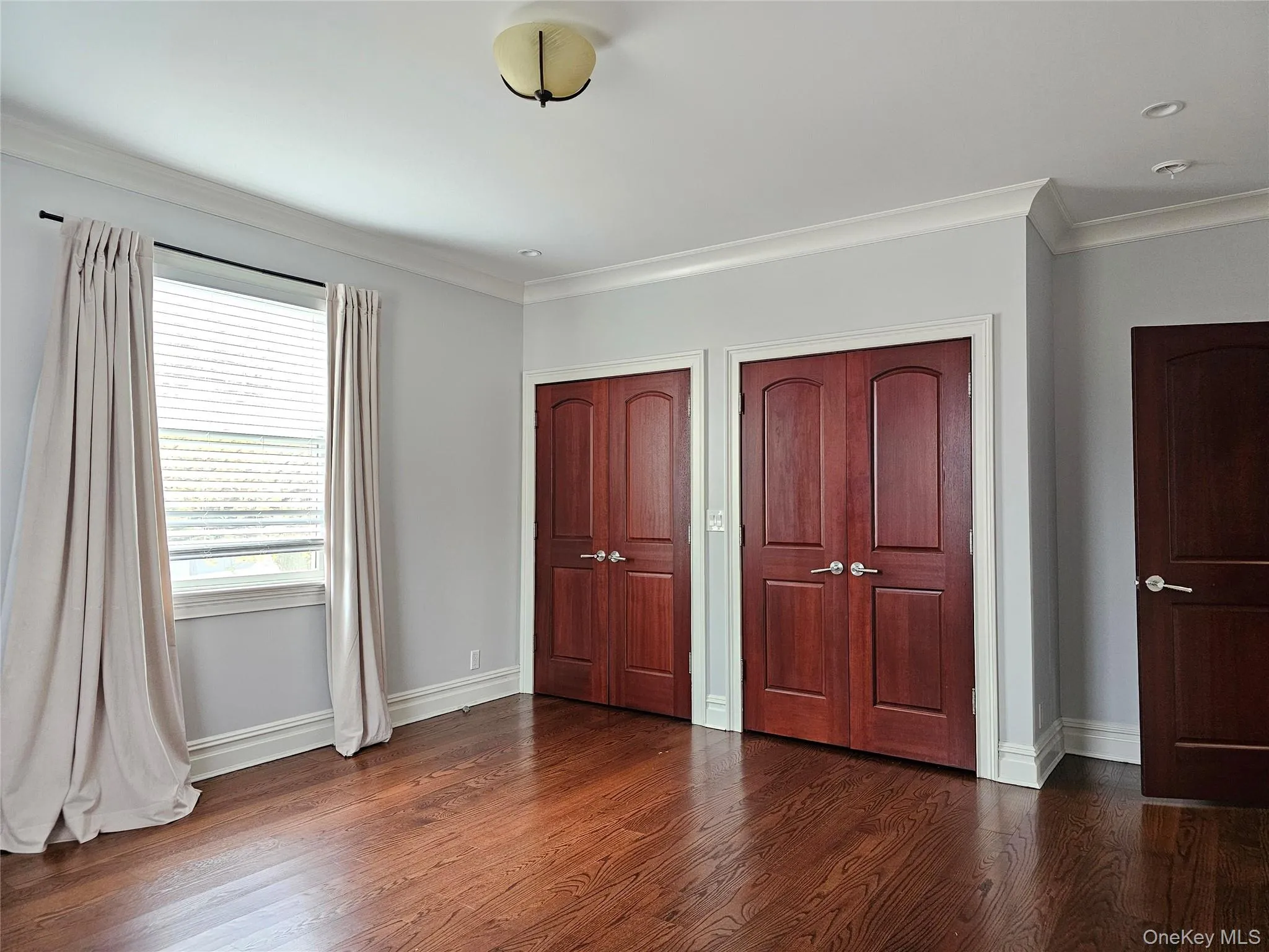 Unfurnished bedroom featuring ornamental molding, multiple closets, and dark wood-style flooring Unfurnished bedroom featuring ornamental molding, multiple closets, and dark wood-style flooring
