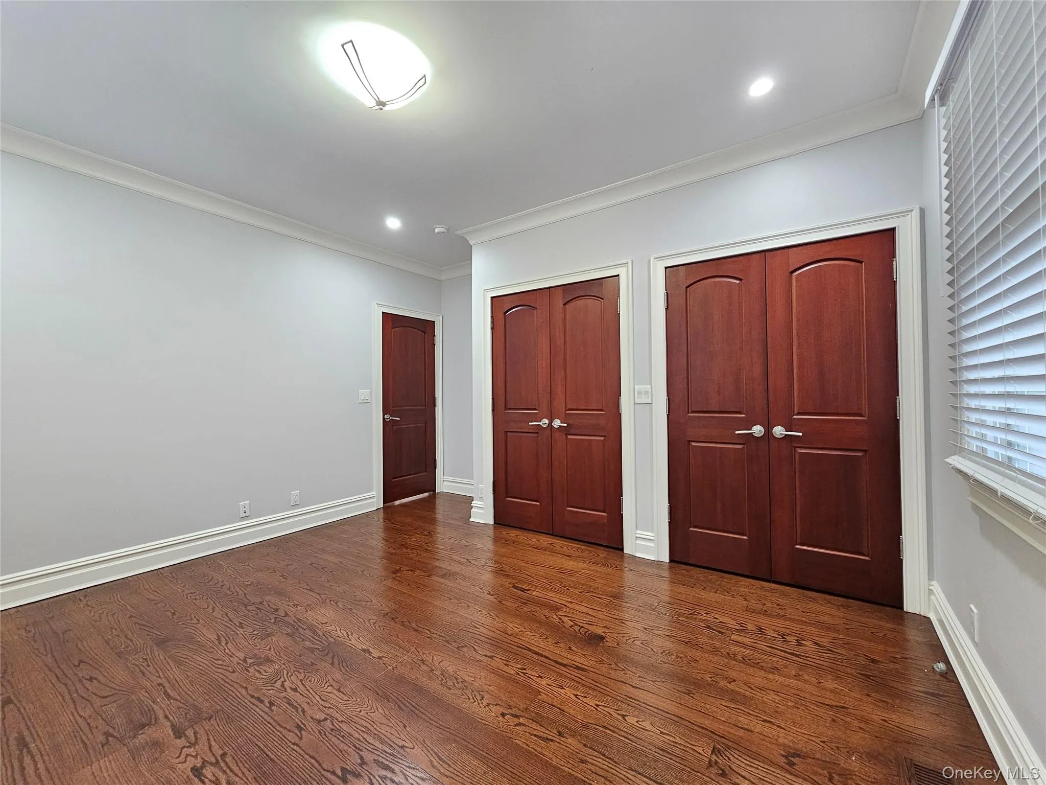 Unfurnished bedroom with multiple closets, crown molding, dark wood-style flooring, and recessed lighting Unfurnished bedroom with multiple closets, crown molding, dark wood-style flooring, and recessed lighting
