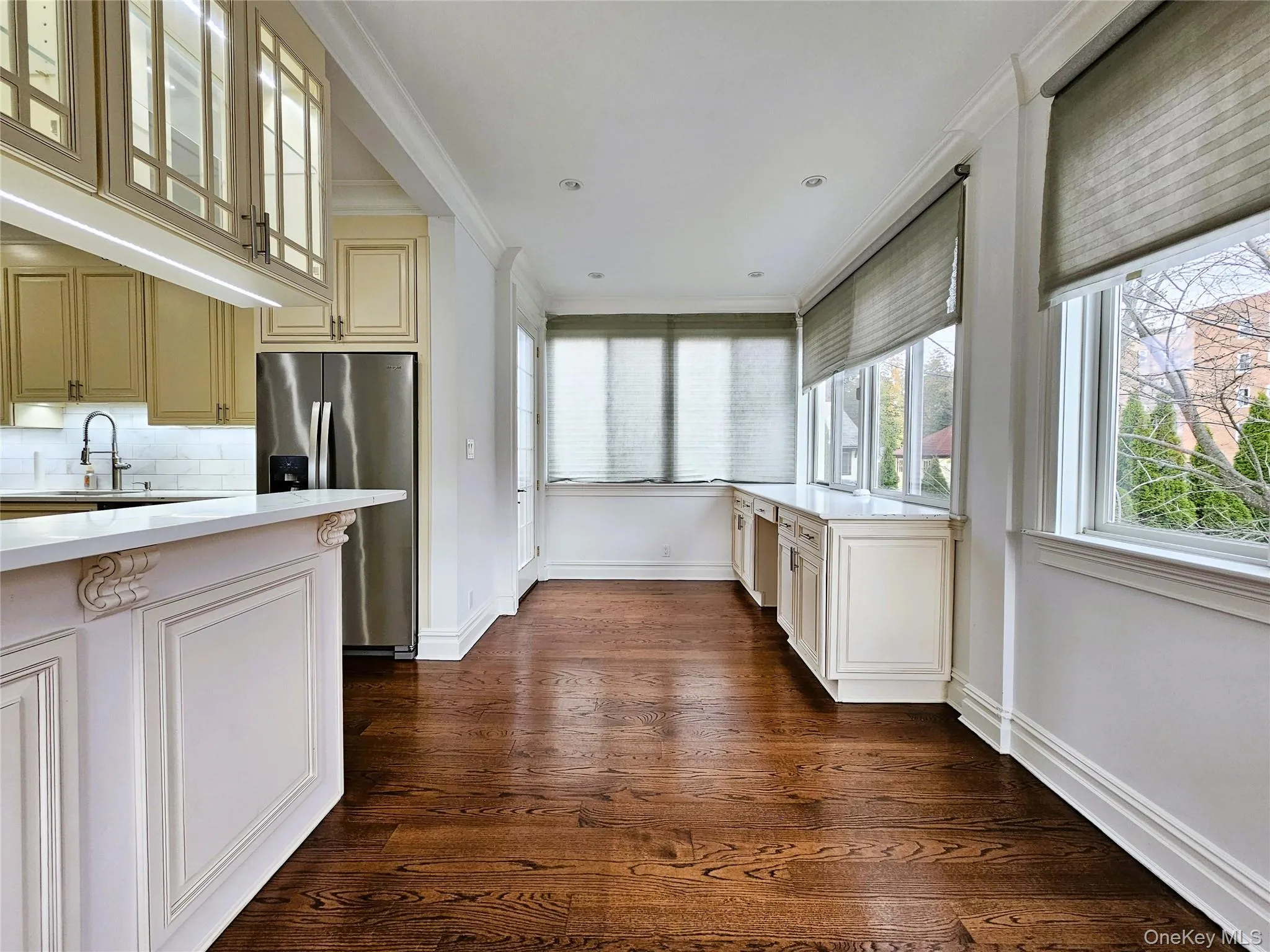Kitchen with stainless steel fridge with ice dispenser, decorative backsplash, dark wood-type flooring, light stone countertops, and ornamental molding Kitchen with stainless steel fridge with ice dispenser, decorative backsplash, dark wood-type flooring, light stone countertops, and ornamental molding