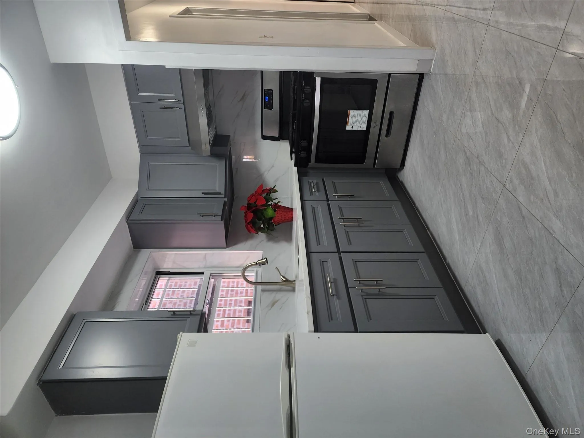 Kitchen with gray cabinetry, fridge, range, and light marble finish flooring Kitchen with gray cabinetry, fridge, range, and light marble finish flooring