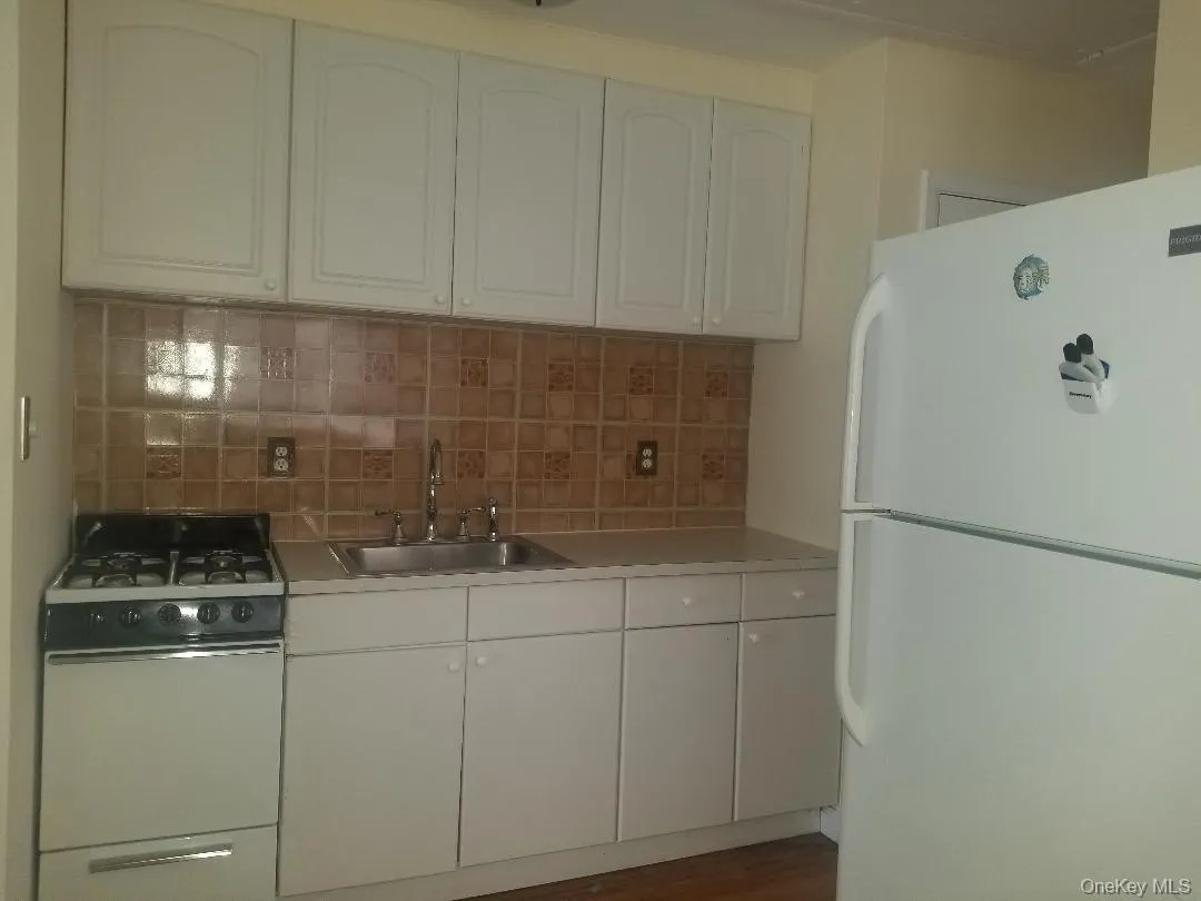 Kitchen with white appliances, light countertops, tasteful backsplash, white cabinetry, and dark wood-style flooring Kitchen with white appliances, light countertops, tasteful backsplash, white cabinetry, and dark wood-style flooring