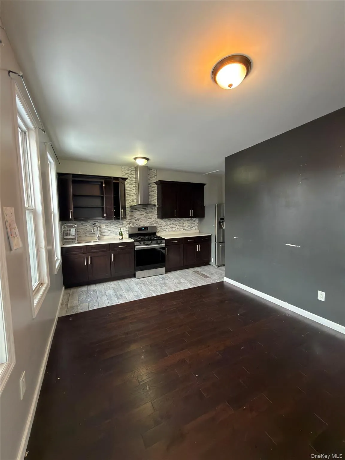 Kitchen with light countertops, appliances with stainless steel finishes, dark wood-style flooring, dark brown cabinetry, and wall chimney range hood Kitchen with light countertops, appliances with stainless steel finishes, dark wood-style flooring, dark brown cabinetry, and wall chimney range hood