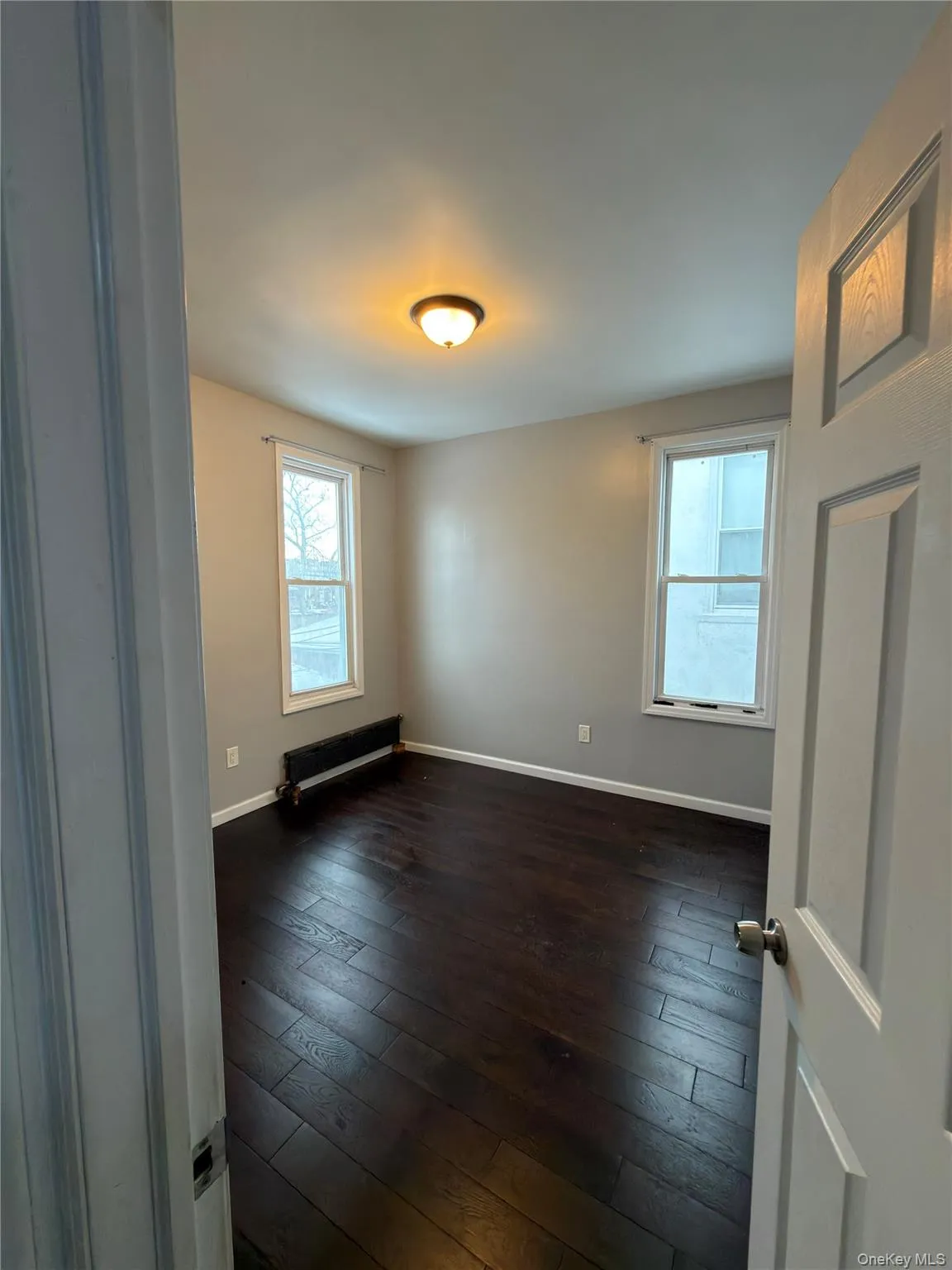 Unfurnished room with dark wood finished floors, healthy amount of natural light, and baseboard heating Unfurnished room with dark wood finished floors, healthy amount of natural light, and baseboard heating