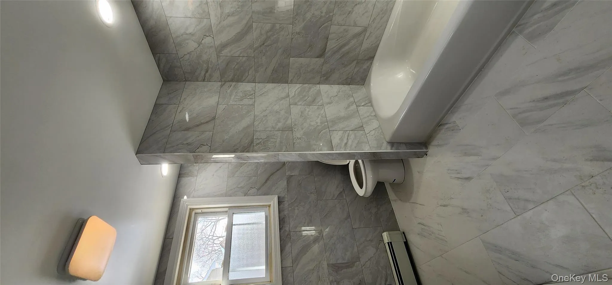 Full bath with tile walls, marble finish floors, and a baseboard heating unit Full bath with tile walls, marble finish floors, and a baseboard heating unit
