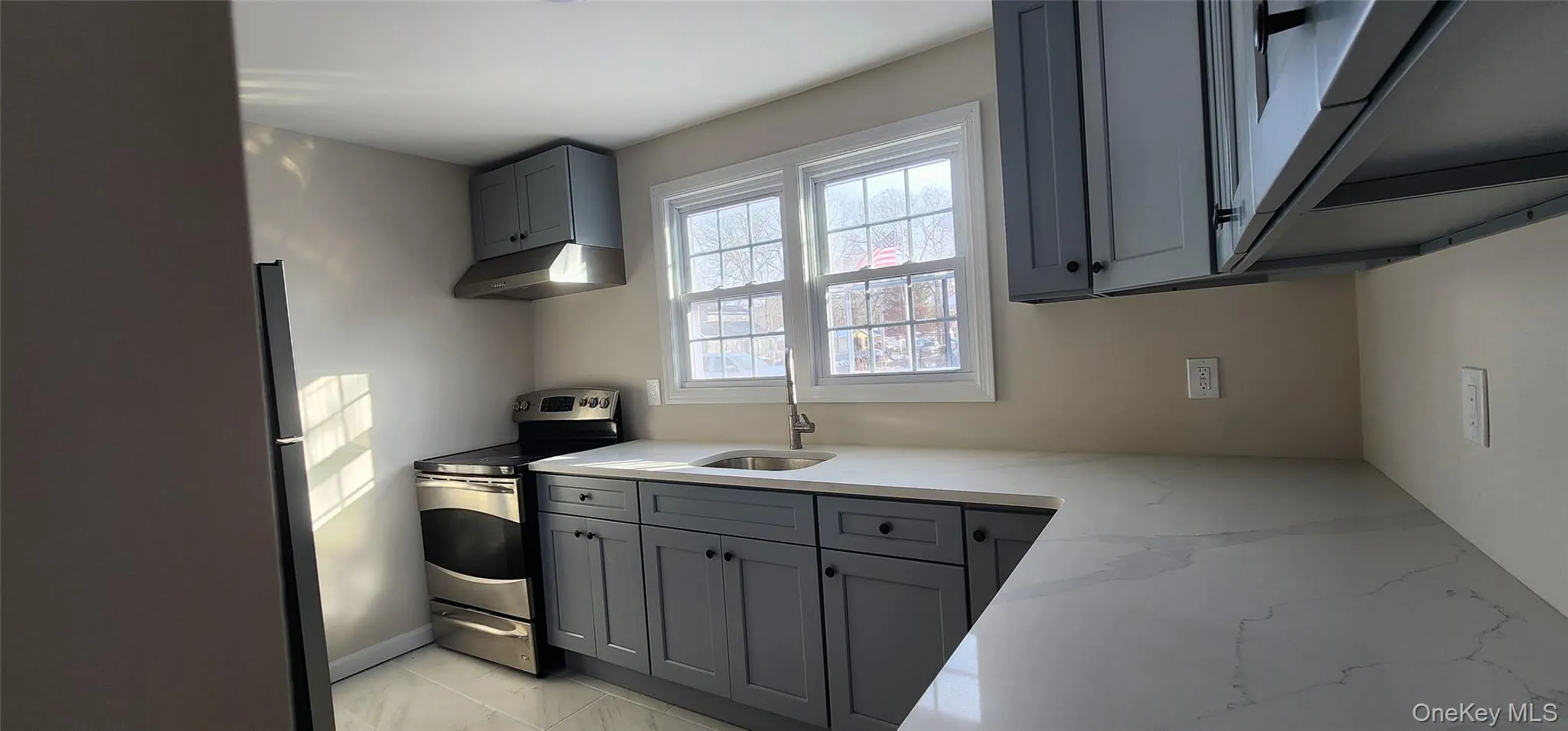 Kitchen featuring gray cabinetry, appliances with stainless steel finishes, light marble finish flooring, and light stone counters Kitchen featuring gray cabinetry, appliances with stainless steel finishes, light marble finish flooring, and light stone counters