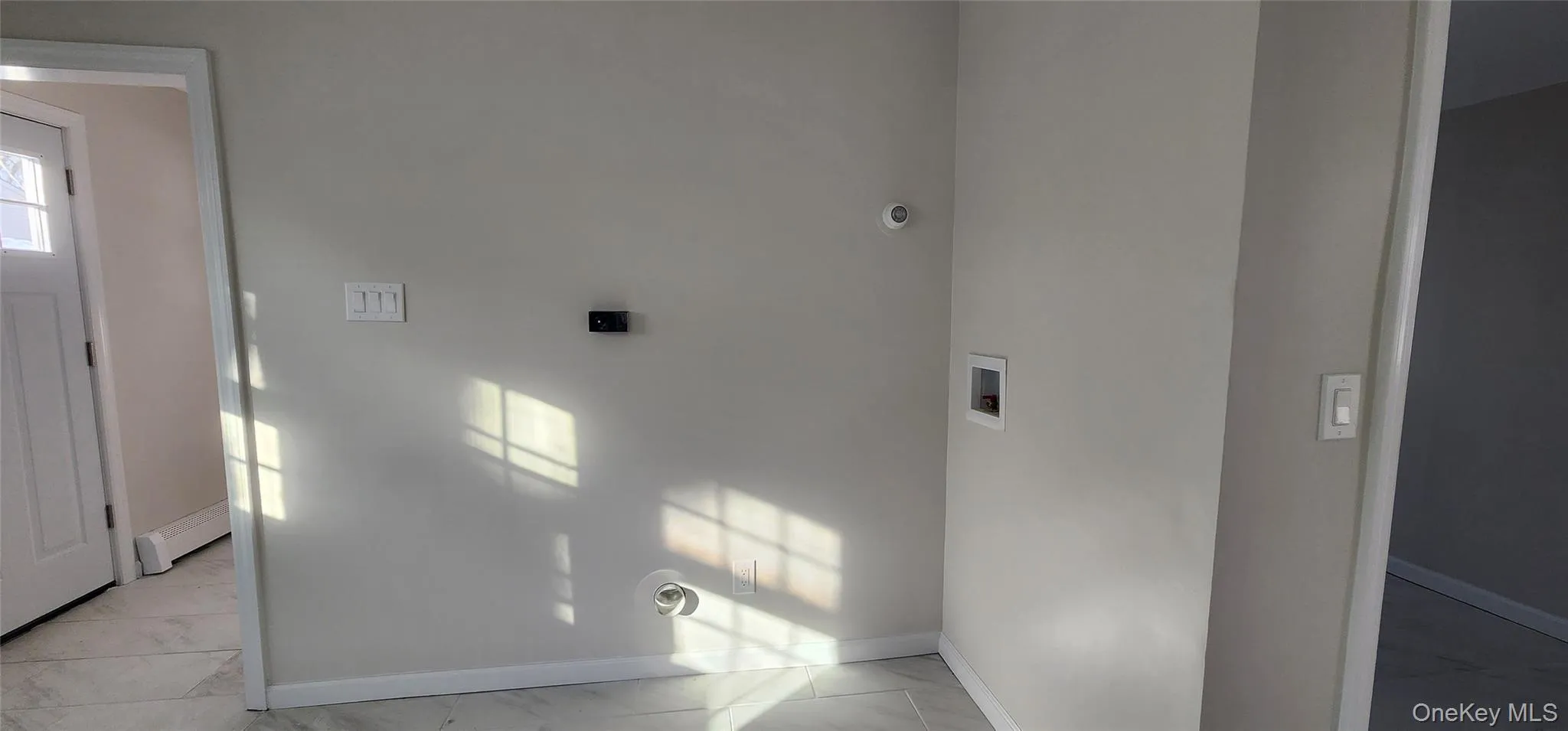 Laundry area featuring washer hookup, baseboard heating, and light marble finish flooring Laundry area featuring washer hookup, baseboard heating, and light marble finish flooring