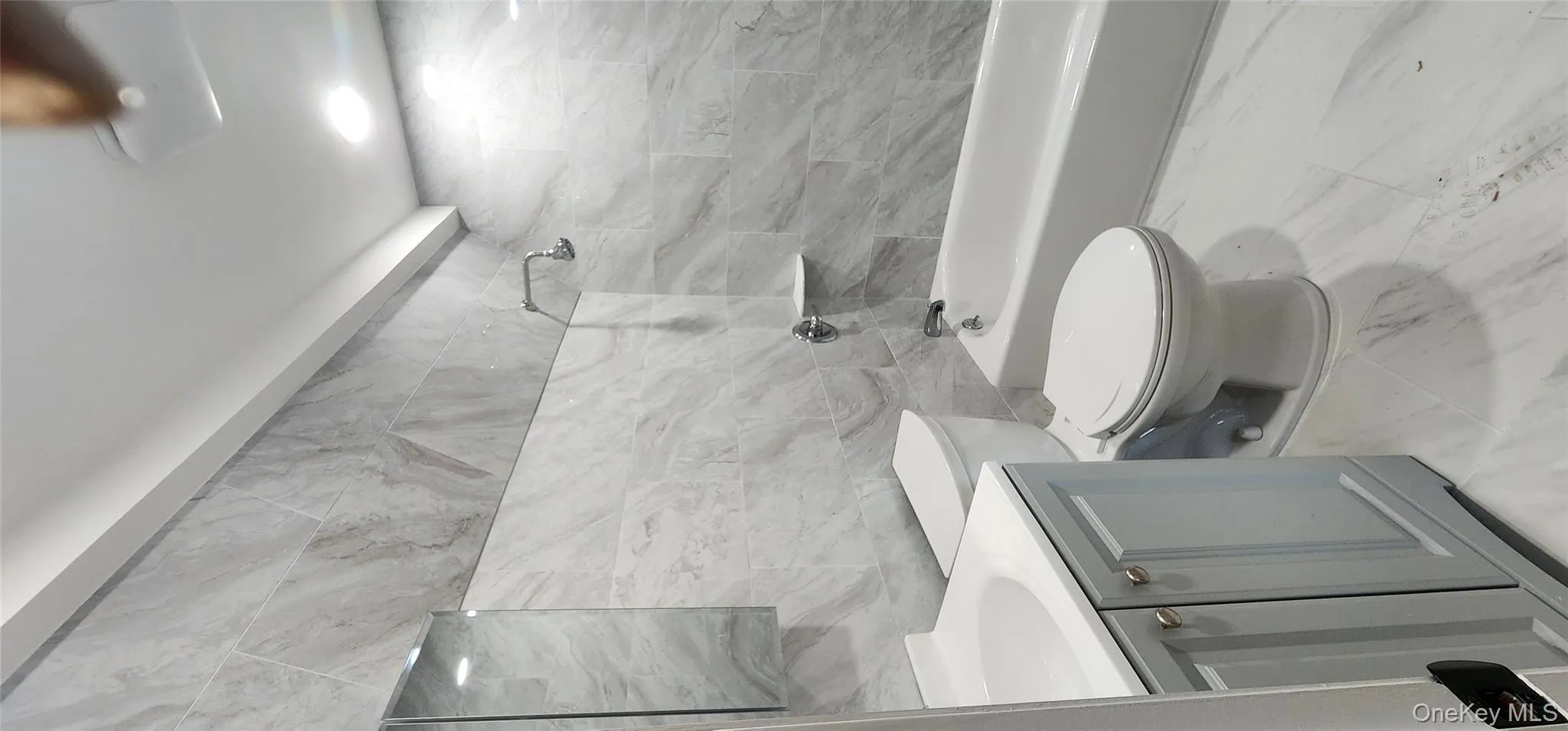 Full bathroom with tile walls, vanity, light marble finish floors, and washtub / shower combination Full bathroom with tile walls, vanity, light marble finish floors, and washtub / shower combination