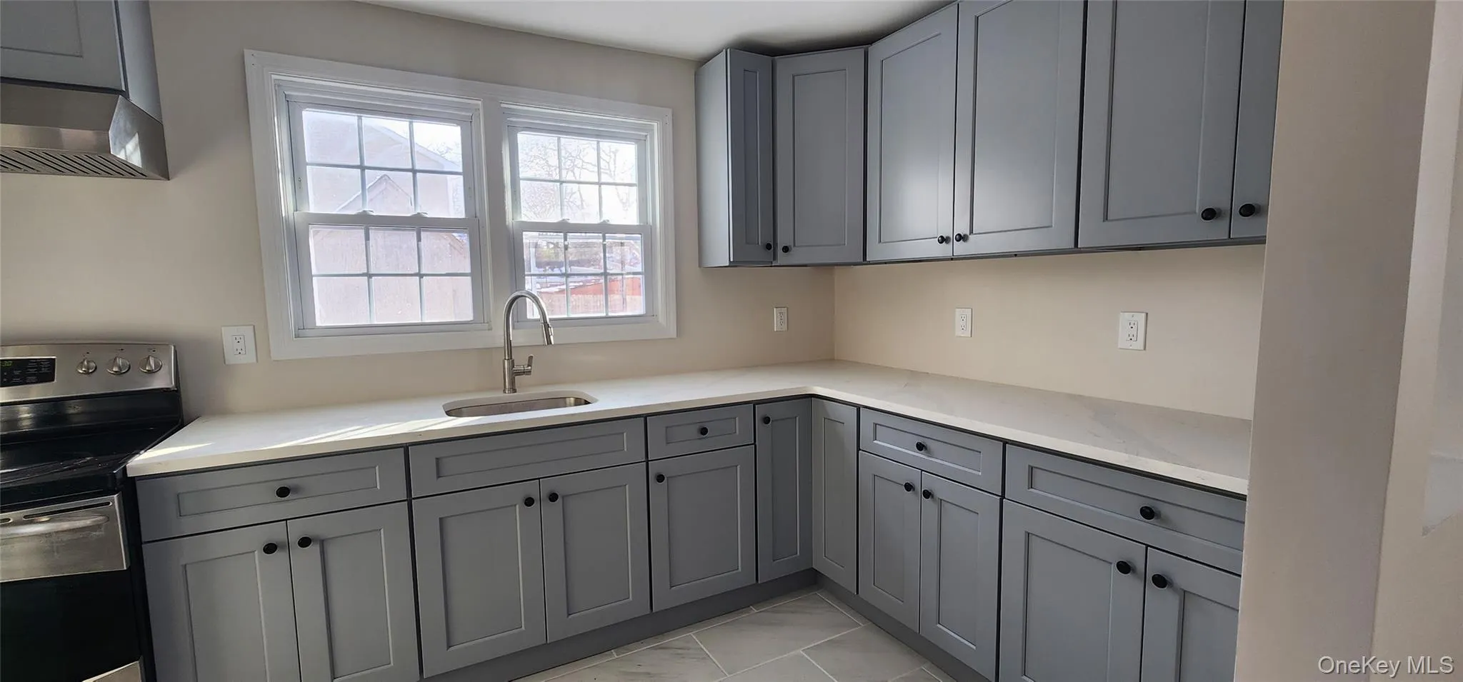 Kitchen featuring stainless steel range with electric stovetop, gray cabinetry, light stone countertops, and under cabinet range hood Kitchen featuring stainless steel range with electric stovetop, gray cabinetry, light stone countertops, and under cabinet range hood