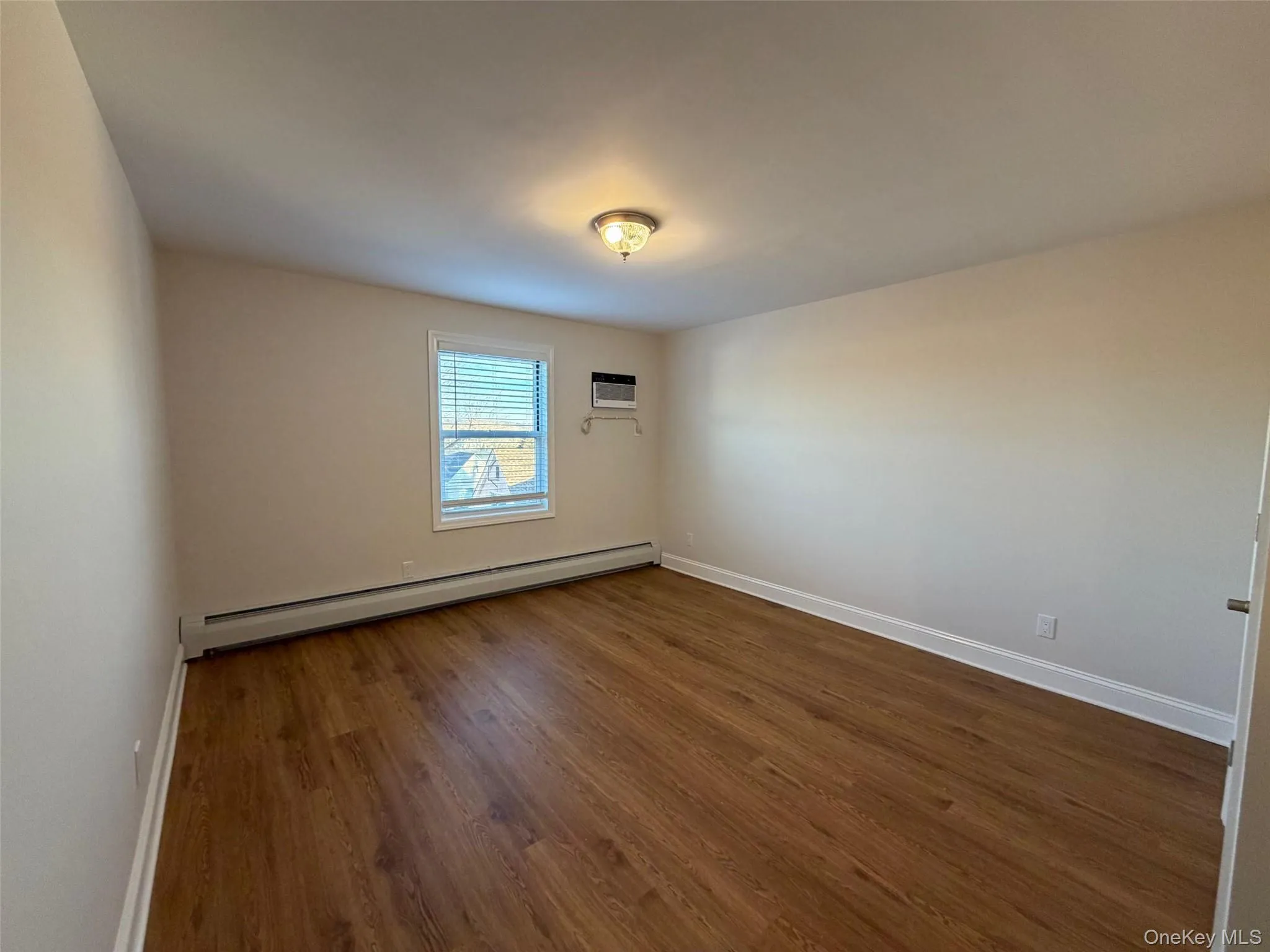 Empty room with baseboard heating and dark wood finished floors Empty room with baseboard heating and dark wood finished floors