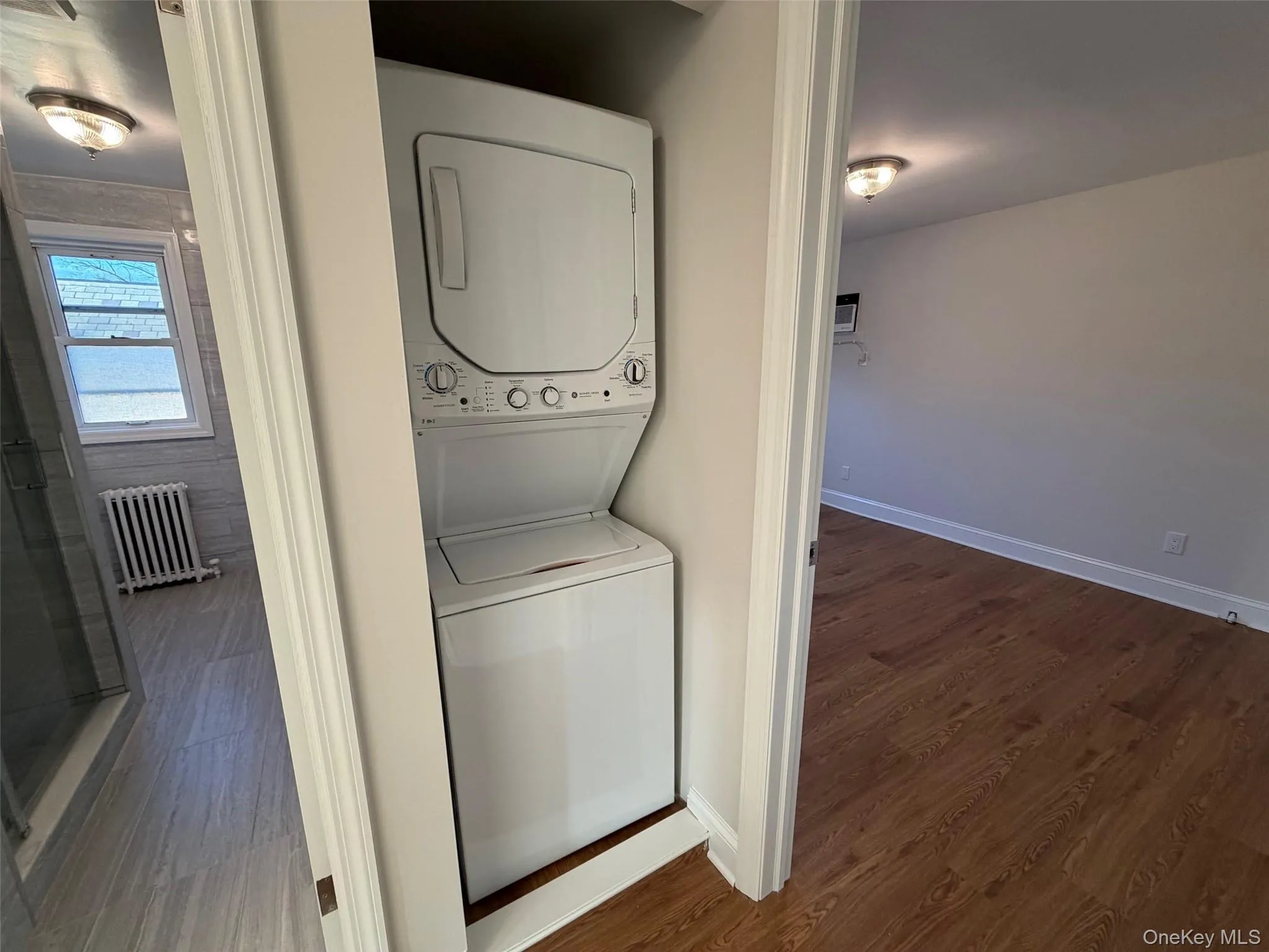 Laundry room featuring radiator, stacked washer / dryer, and dark wood-style flooring Laundry room featuring radiator, stacked washer / dryer, and dark wood-style flooring
