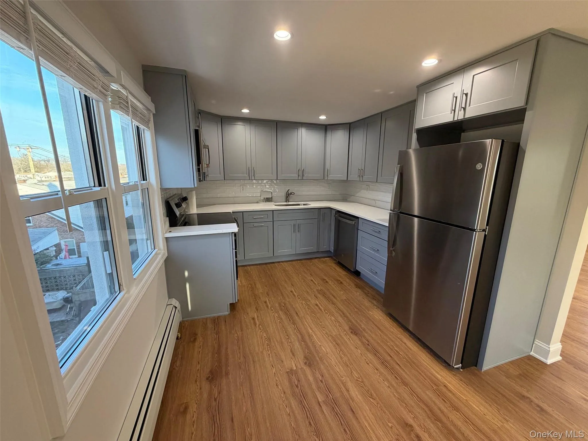 Kitchen featuring gray cabinets, a baseboard heating unit, stainless steel appliances, light wood finished floors, and backsplash Kitchen featuring gray cabinets, a baseboard heating unit, stainless steel appliances, light wood finished floors, and backsplash