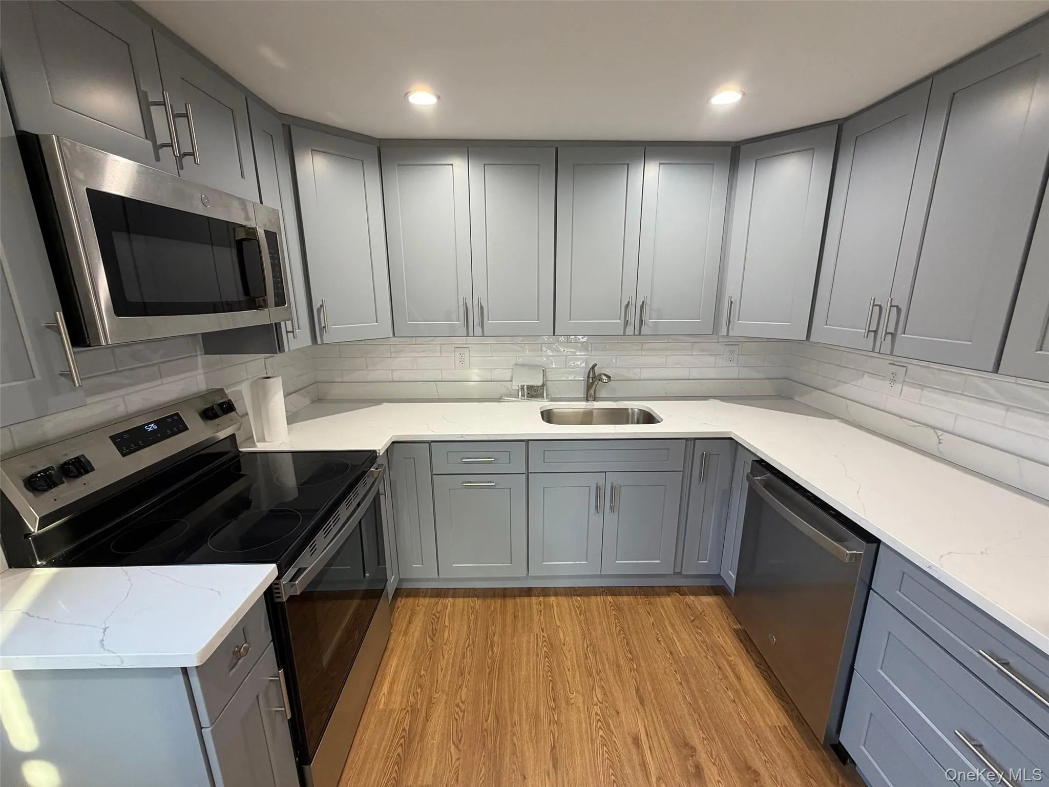 Kitchen featuring gray cabinets, appliances with stainless steel finishes, light stone countertops, and light wood finished floors Kitchen featuring gray cabinets, appliances with stainless steel finishes, light stone countertops, and light wood finished floors