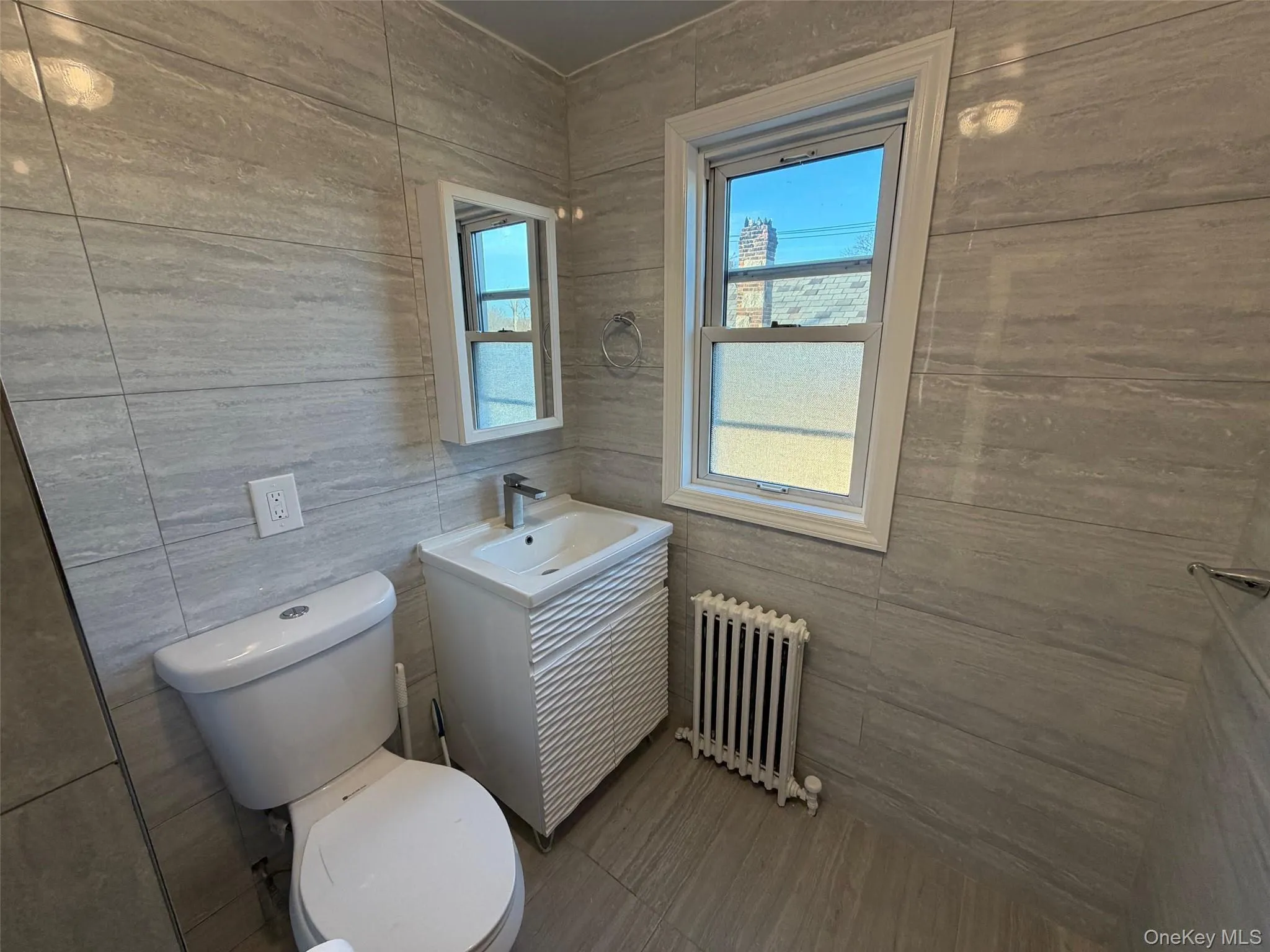 Half bath with radiator, vanity, tile patterned flooring, and tile walls Half bath with radiator, vanity, tile patterned flooring, and tile walls