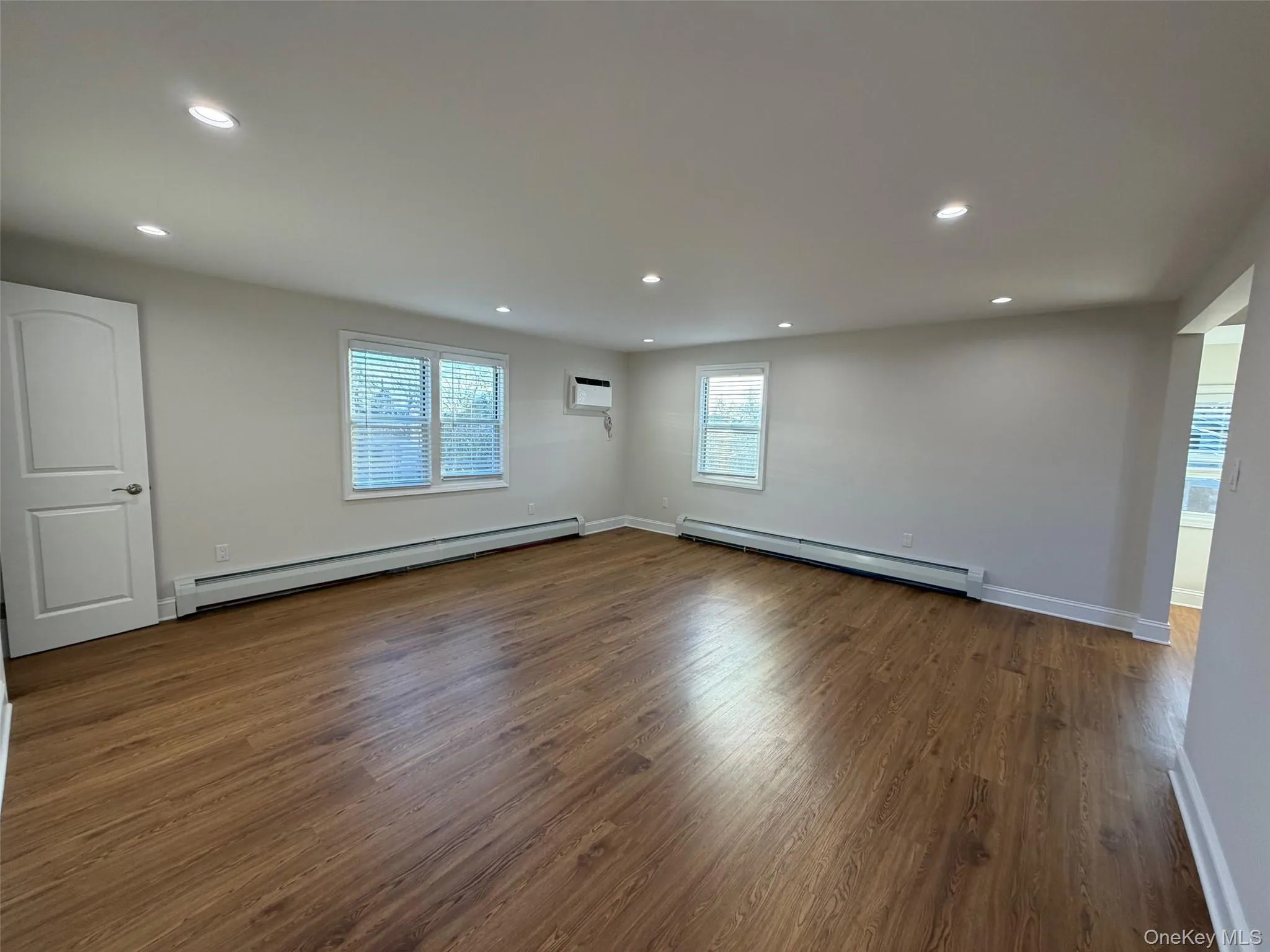 Unfurnished room featuring a baseboard heating unit, baseboard heating, dark wood-style flooring, recessed lighting, and a wall mounted air conditioner Unfurnished room featuring a baseboard heating unit, baseboard heating, dark wood-style flooring, recessed lighting, and a wall mounted air conditioner
