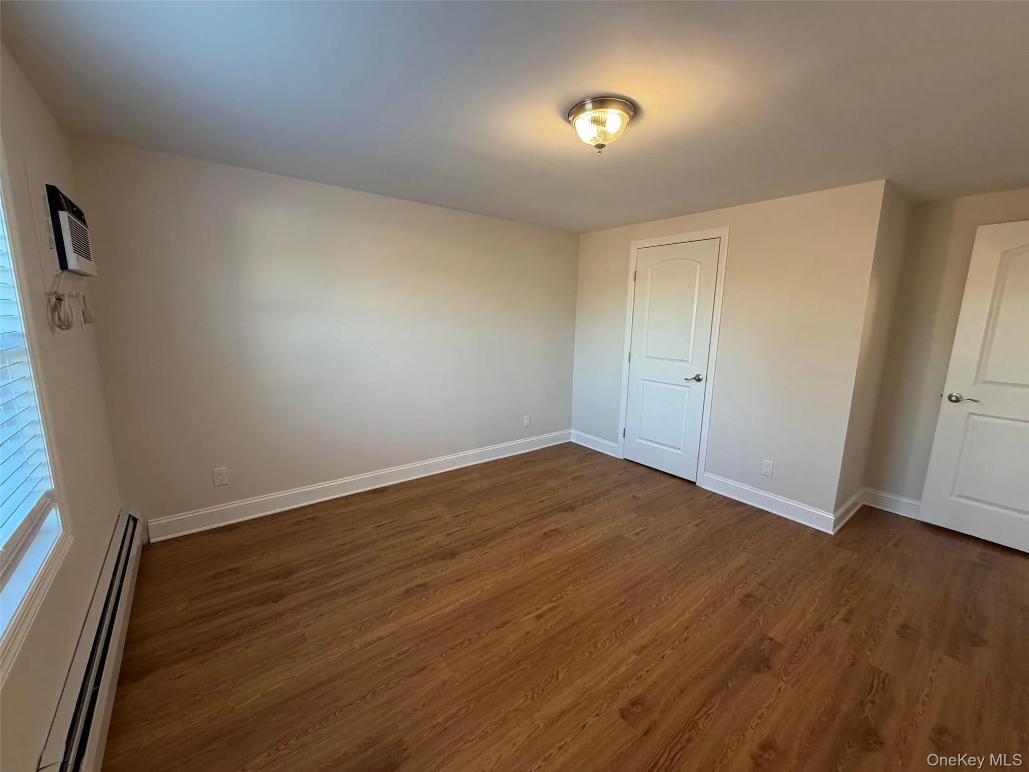Unfurnished bedroom with baseboard heating and dark wood finished floors Unfurnished bedroom with baseboard heating and dark wood finished floors