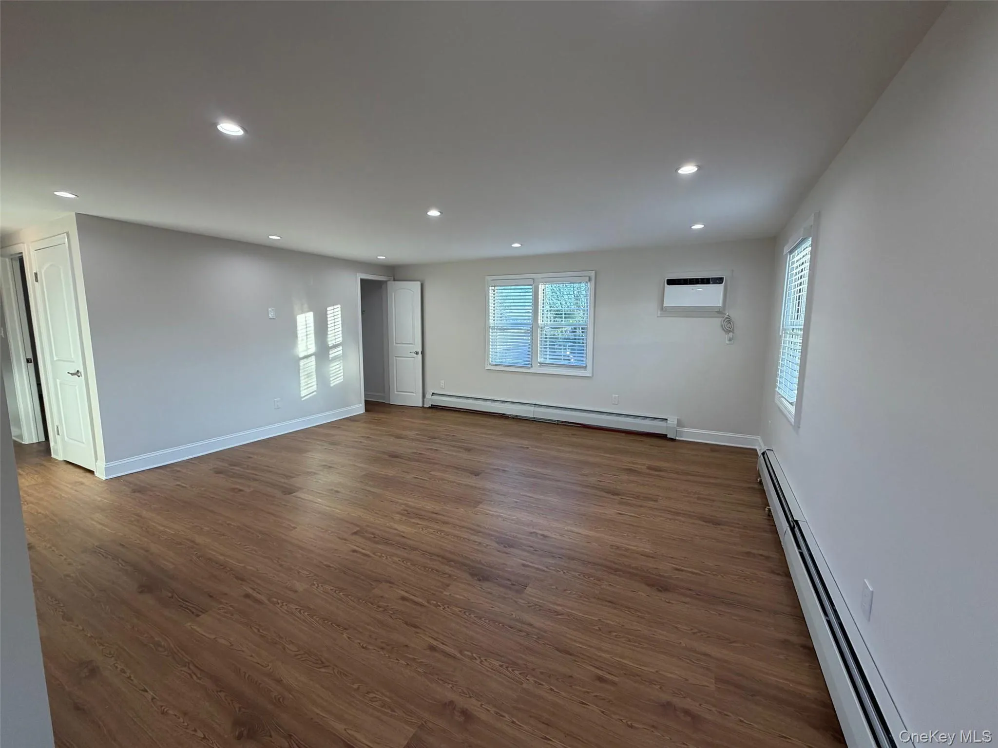 Empty room with a baseboard heating unit, recessed lighting, dark wood-style floors, and a wall unit AC Empty room with a baseboard heating unit, recessed lighting, dark wood-style floors, and a wall unit AC
