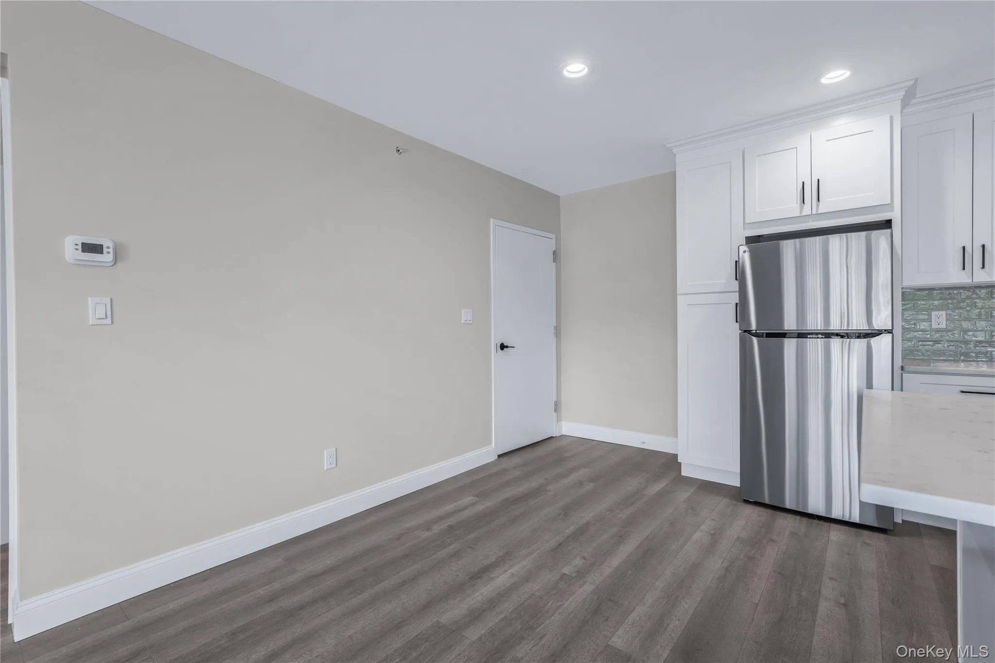 Kitchen featuring freestanding refrigerator, white cabinets, backsplash, dark wood-style floors, and light stone countertops Kitchen featuring freestanding refrigerator, white cabinets, backsplash, dark wood-style floors, and light stone countertops