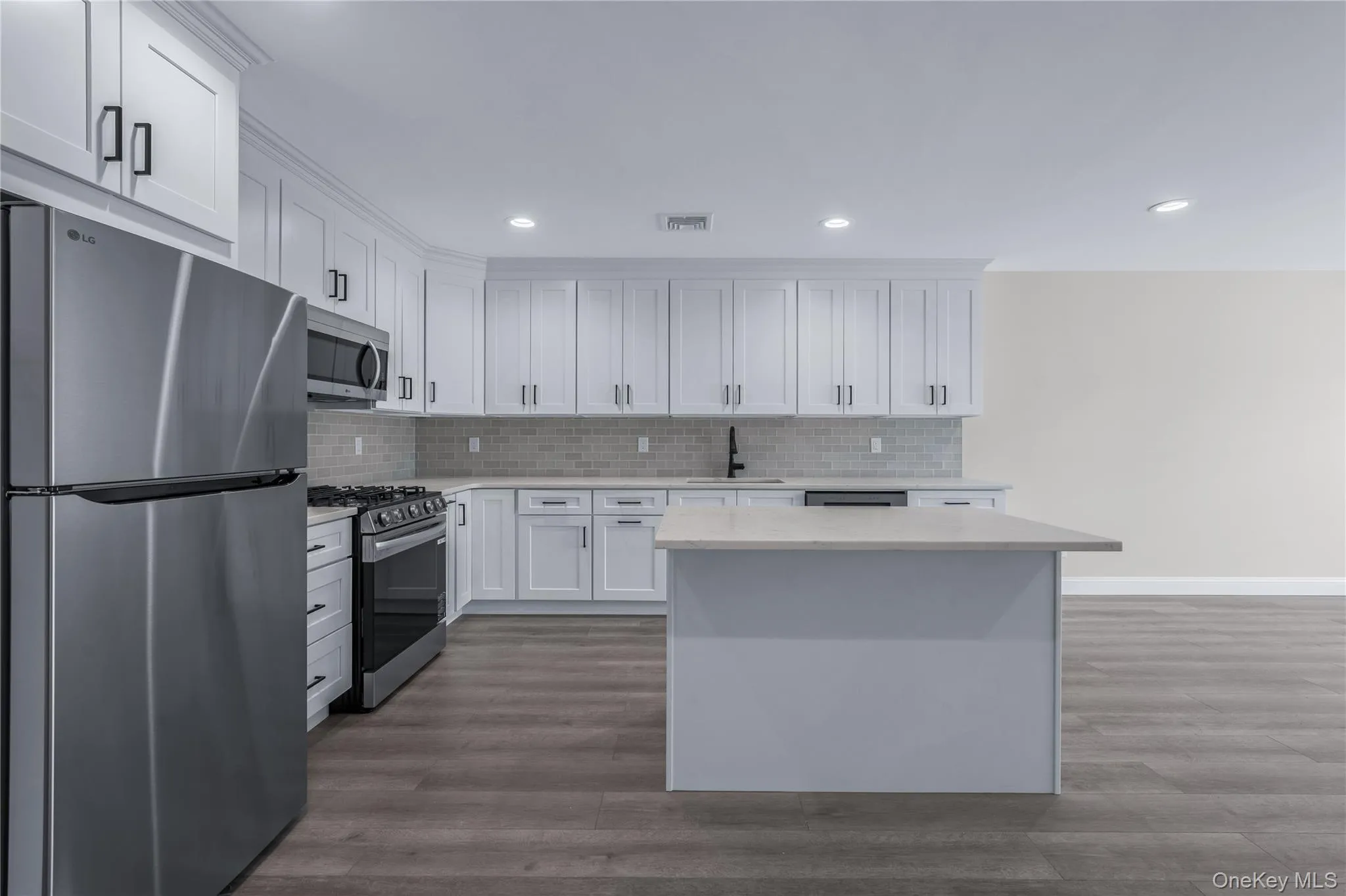 Kitchen featuring appliances with stainless steel finishes, white cabinetry, dark wood finished floors, a center island, and light stone countertops Kitchen featuring appliances with stainless steel finishes, white cabinetry, dark wood finished floors, a center island, and light stone countertops