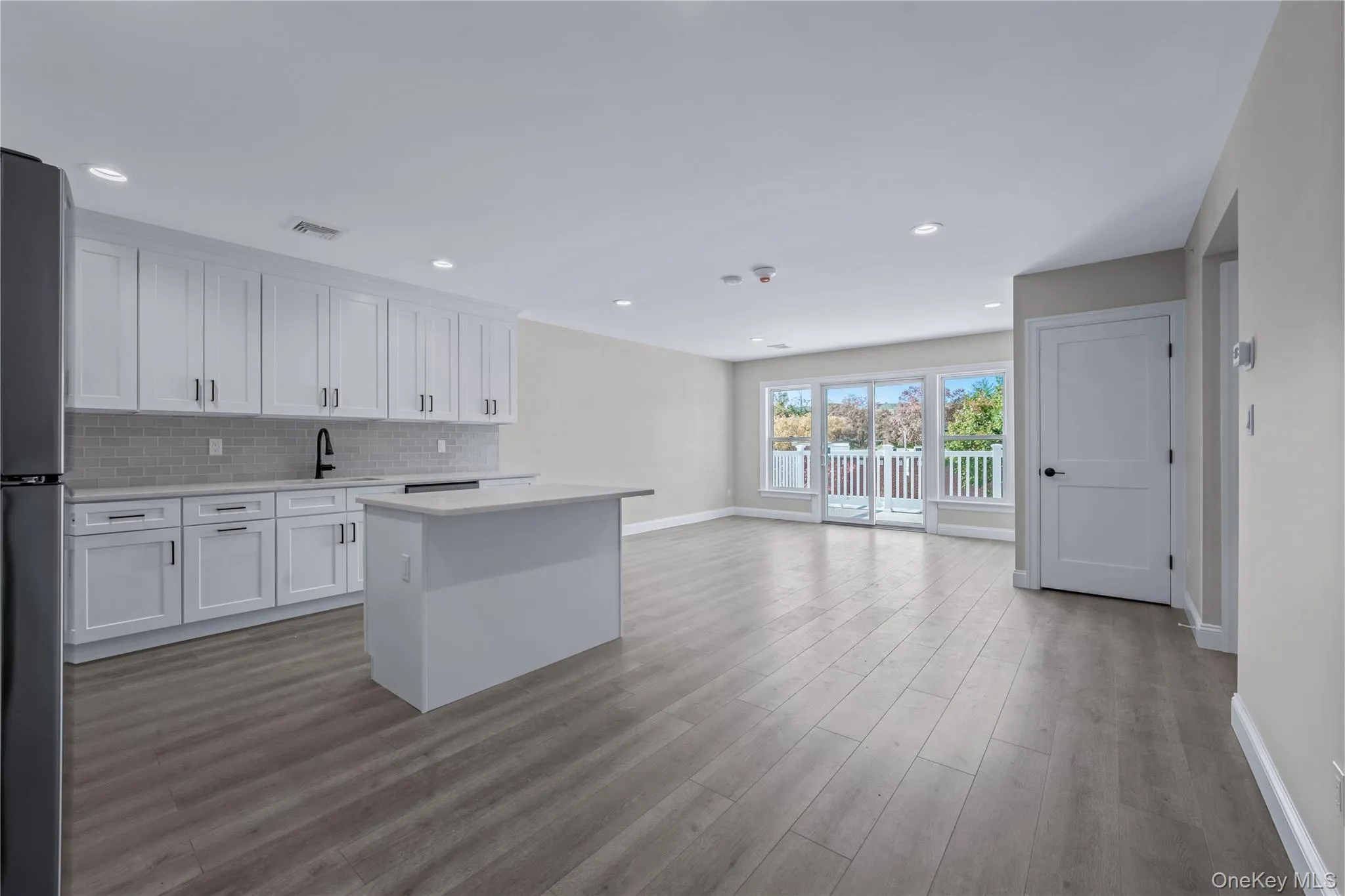 Kitchen featuring white cabinets, a kitchen island, freestanding refrigerator, open floor plan, and light wood-type flooring Kitchen featuring white cabinets, a kitchen island, freestanding refrigerator, open floor plan, and light wood-type flooring
