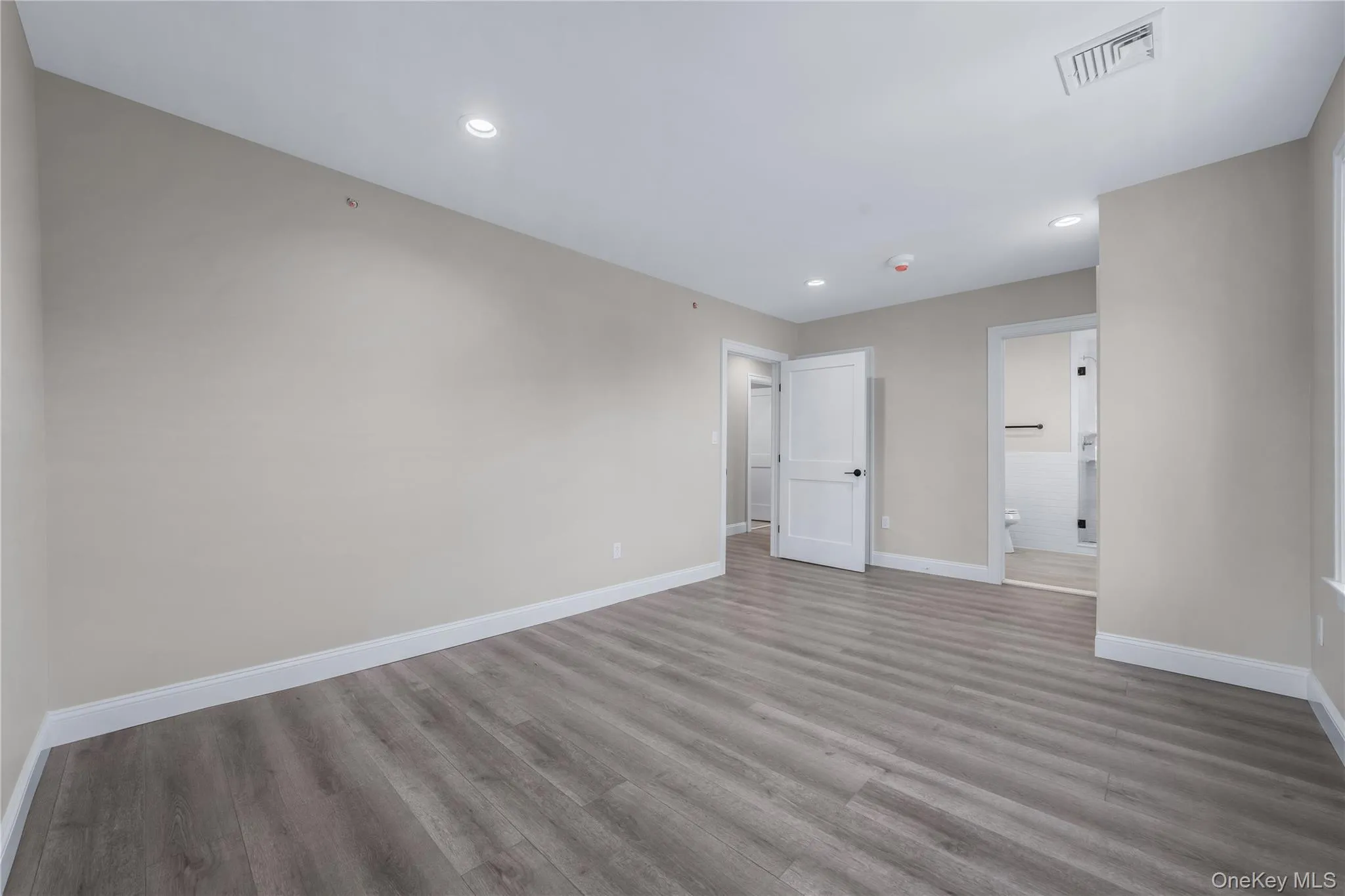 Unfurnished bedroom with recessed lighting, light wood-style flooring, and ensuite bathroom Unfurnished bedroom with recessed lighting, light wood-style flooring, and ensuite bathroom