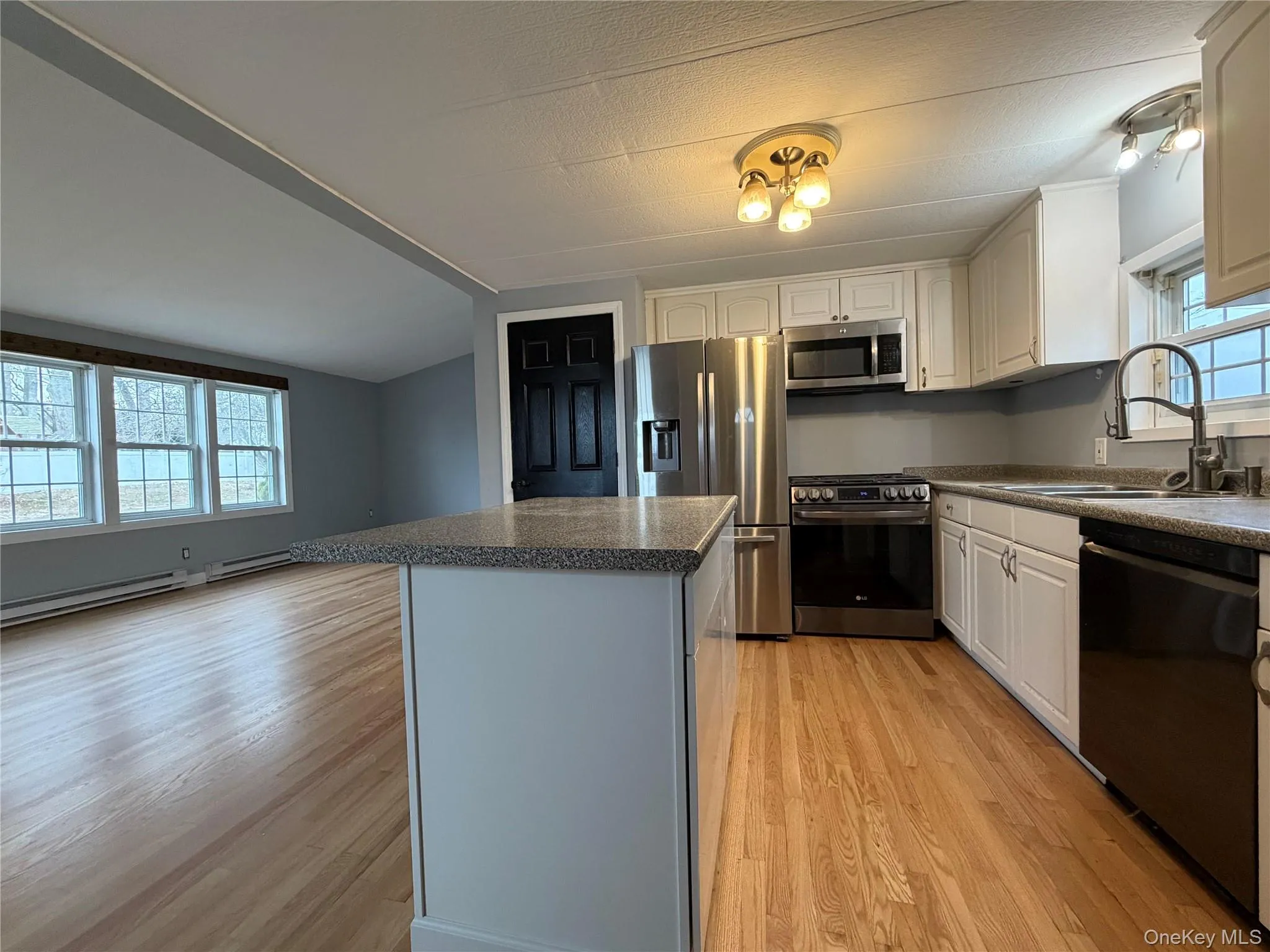 Kitchen featuring stainless steel appliances, dark countertops, a kitchen island, and white cabinetry Kitchen featuring stainless steel appliances, dark countertops, a kitchen island, and white cabinetry