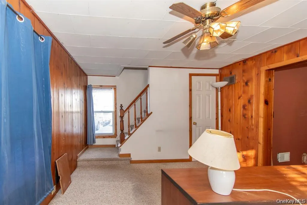 Carpeted foyer featuring wooden walls, stairs, and ceiling fan Carpeted foyer featuring wooden walls, stairs, and ceiling fan