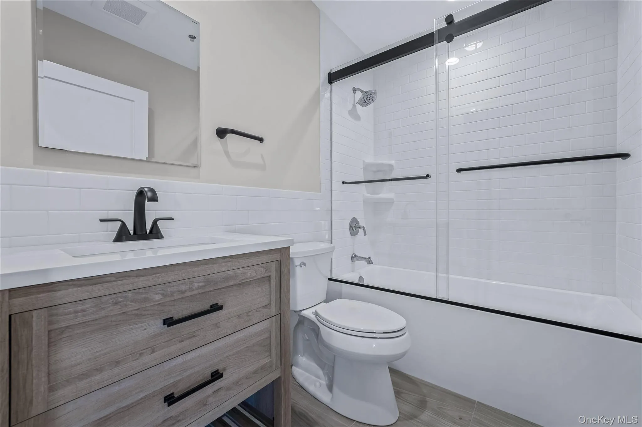 Full bath featuring vanity, combined bath / shower with glass door, tile walls, and a wainscoted wall Full bath featuring vanity, combined bath / shower with glass door, tile walls, and a wainscoted wall