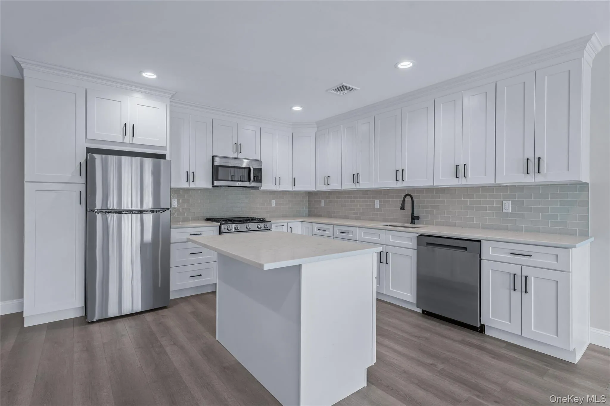 Kitchen with stainless steel appliances, white cabinets, a center island, light wood-style floors, and recessed lighting Kitchen with stainless steel appliances, white cabinets, a center island, light wood-style floors, and recessed lighting