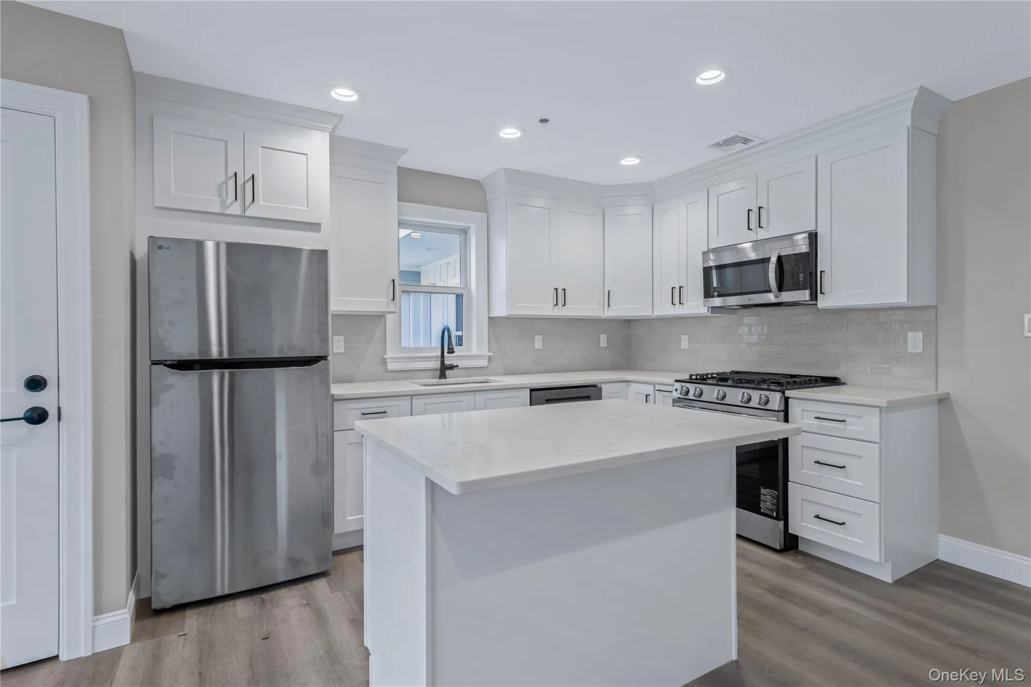 Kitchen featuring appliances with stainless steel finishes, white cabinetry, a center island, light stone counters, and light wood-style flooring Kitchen featuring appliances with stainless steel finishes, white cabinetry, a center island, light stone counters, and light wood-style flooring