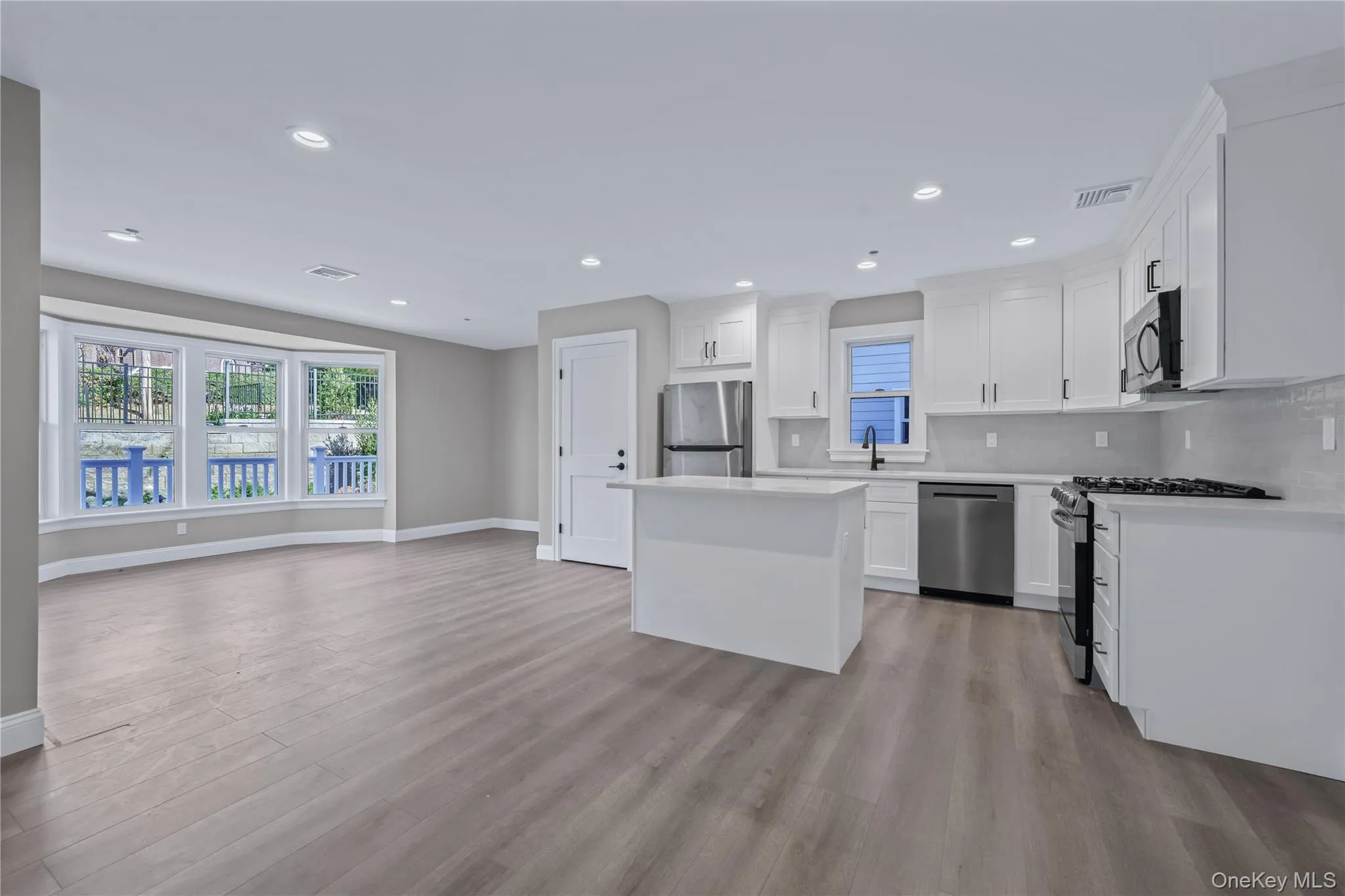 Kitchen featuring white cabinetry, appliances with stainless steel finishes, open floor plan, a center island, and light wood finished floors Kitchen featuring white cabinetry, appliances with stainless steel finishes, open floor plan, a center island, and light wood finished floors