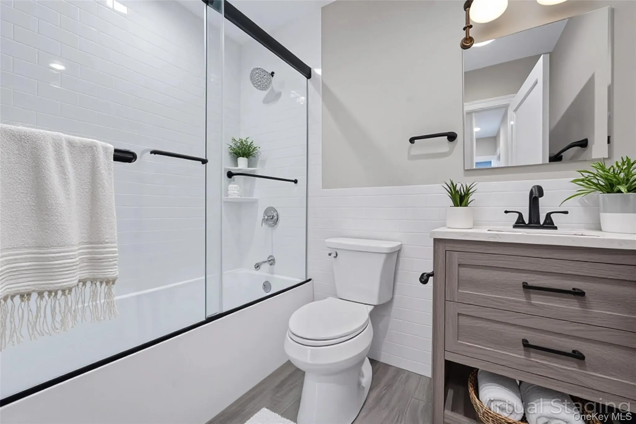 Bathroom with vanity, a wainscoted wall, bath / shower combo with glass door, tile walls, and light wood-style flooring Bathroom with vanity, a wainscoted wall, bath / shower combo with glass door, tile walls, and light wood-style flooring