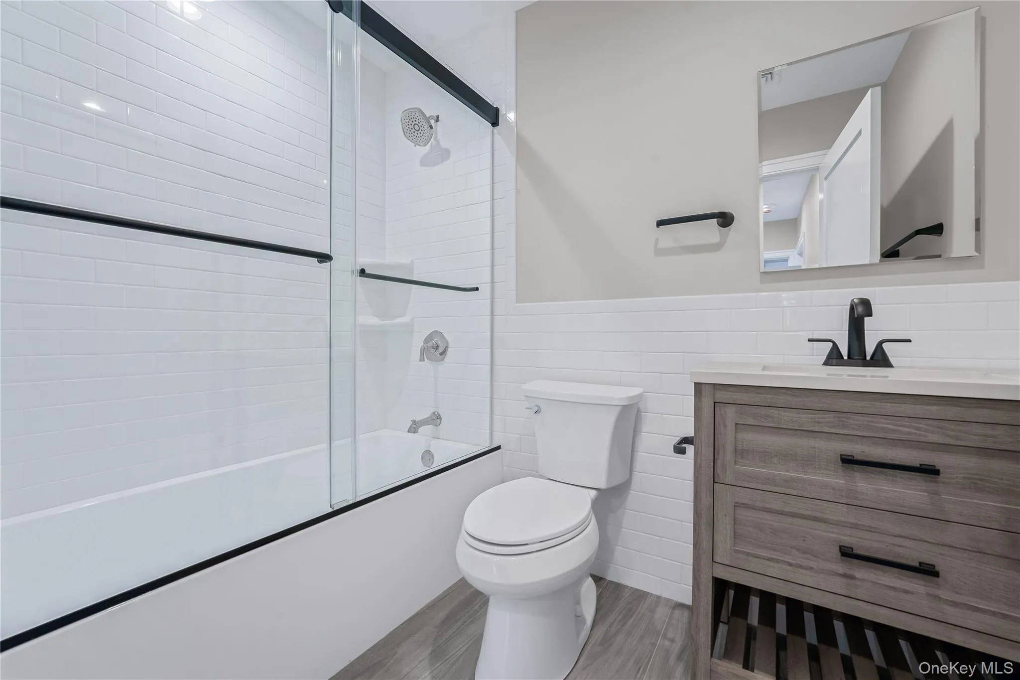 Bathroom with wainscoting, tile walls, vanity, enclosed tub / shower combo, and light wood finished floors Bathroom with wainscoting, tile walls, vanity, enclosed tub / shower combo, and light wood finished floors