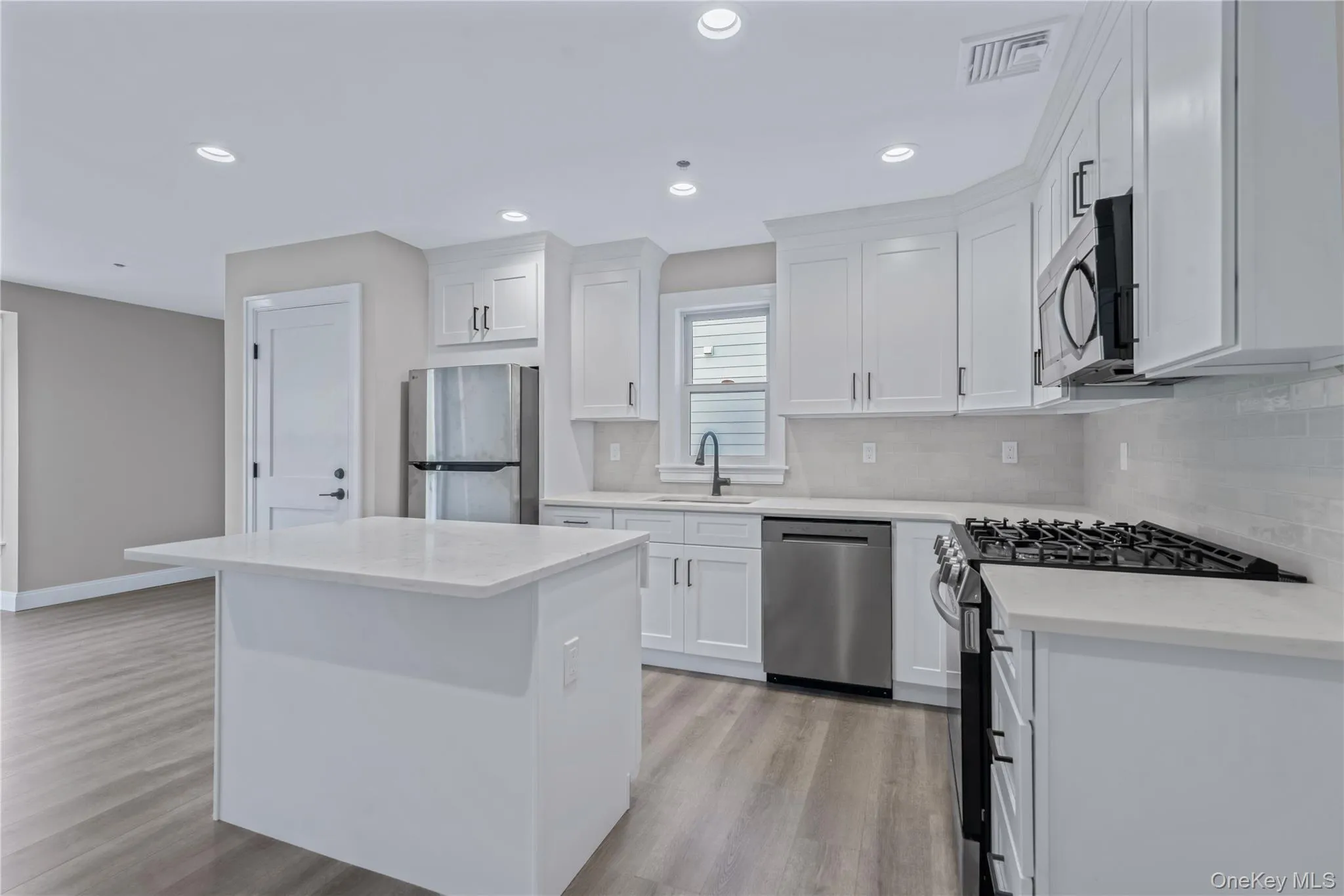 Kitchen featuring stainless steel appliances, white cabinetry, a kitchen island, light wood finished floors, and tasteful backsplash Kitchen featuring stainless steel appliances, white cabinetry, a kitchen island, light wood finished floors, and tasteful backsplash
