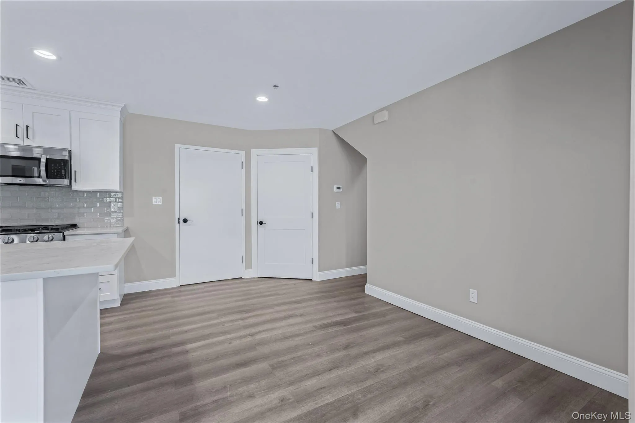 Kitchen with white cabinetry, stainless steel appliances, light stone counters, backsplash, and dark wood-style floors Kitchen with white cabinetry, stainless steel appliances, light stone counters, backsplash, and dark wood-style floors