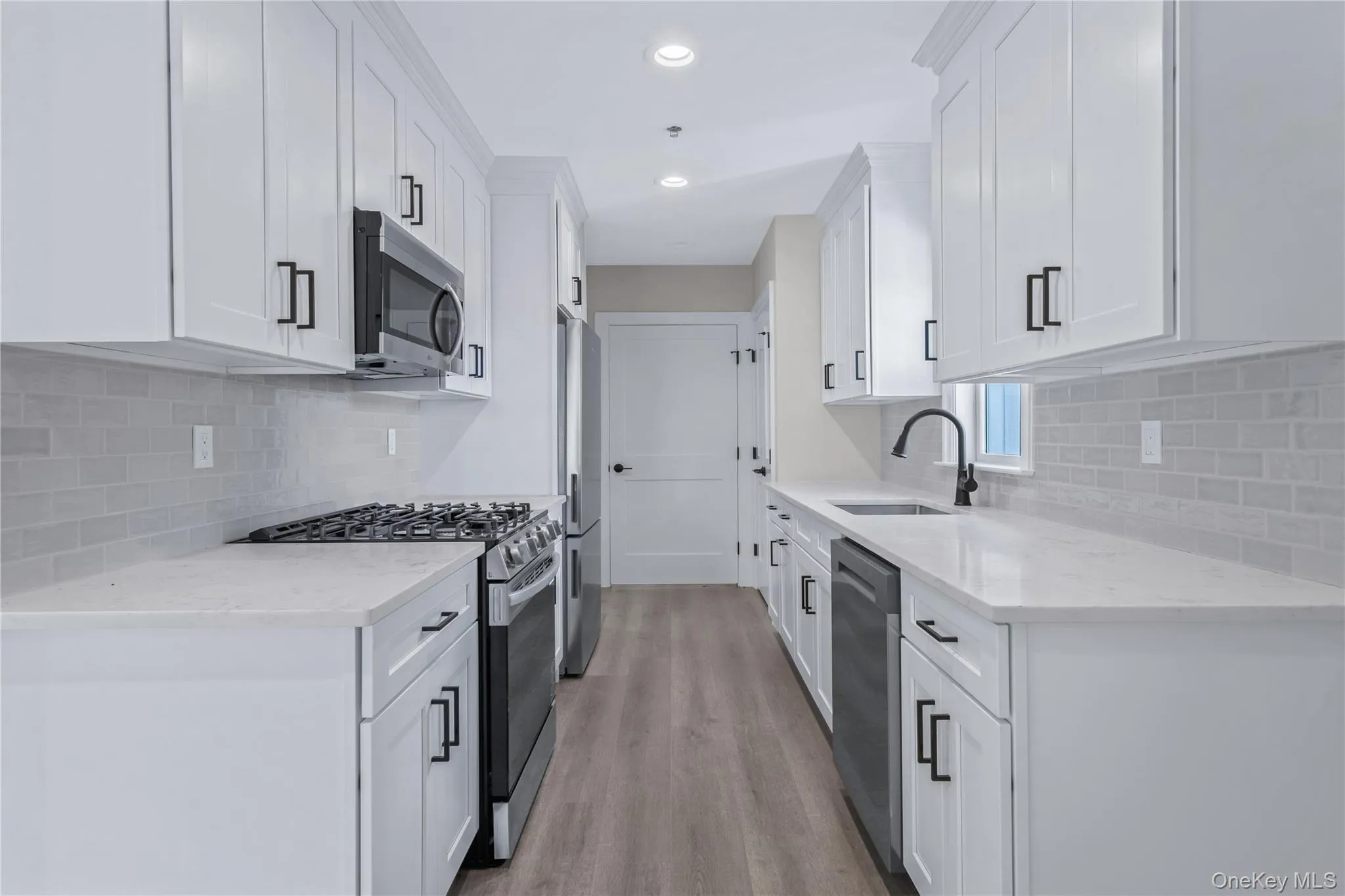 Kitchen featuring appliances with stainless steel finishes, tasteful backsplash, light stone counters, white cabinets, and light wood-style floors Kitchen featuring appliances with stainless steel finishes, tasteful backsplash, light stone counters, white cabinets, and light wood-style floors