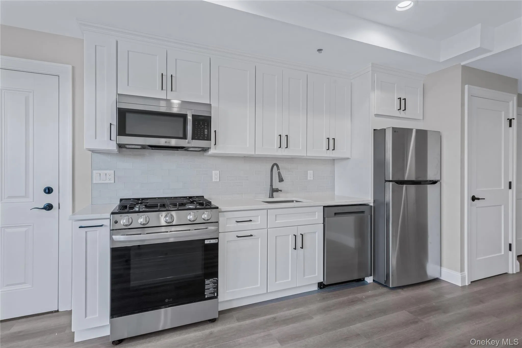 Kitchen with stainless steel appliances, white cabinetry, backsplash, light stone countertops, and recessed lighting Kitchen with stainless steel appliances, white cabinetry, backsplash, light stone countertops, and recessed lighting