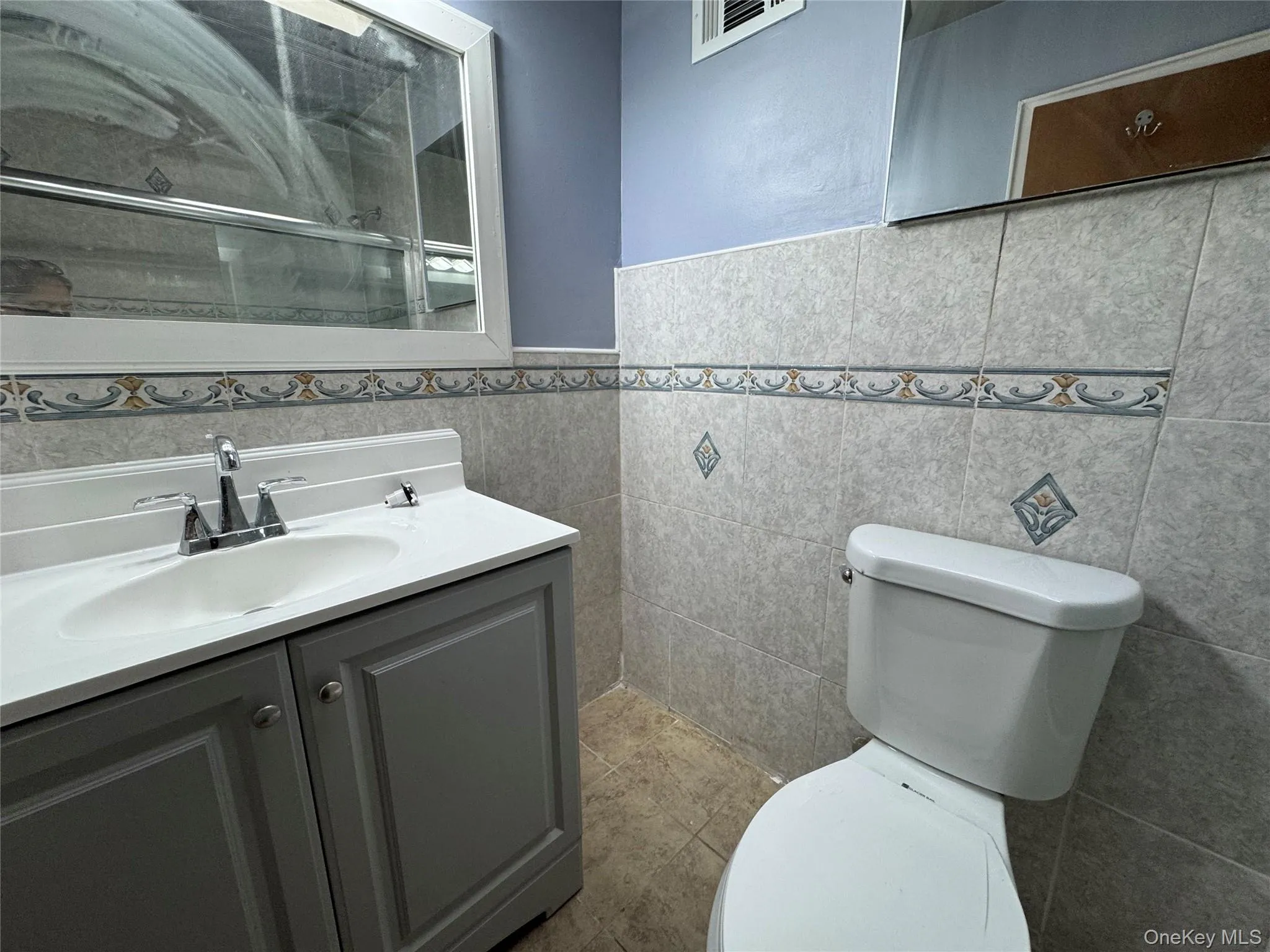 Full bathroom with vanity, tile walls, a wainscoted wall, an enclosed shower, and light tile patterned floors Full bathroom with vanity, tile walls, a wainscoted wall, an enclosed shower, and light tile patterned floors