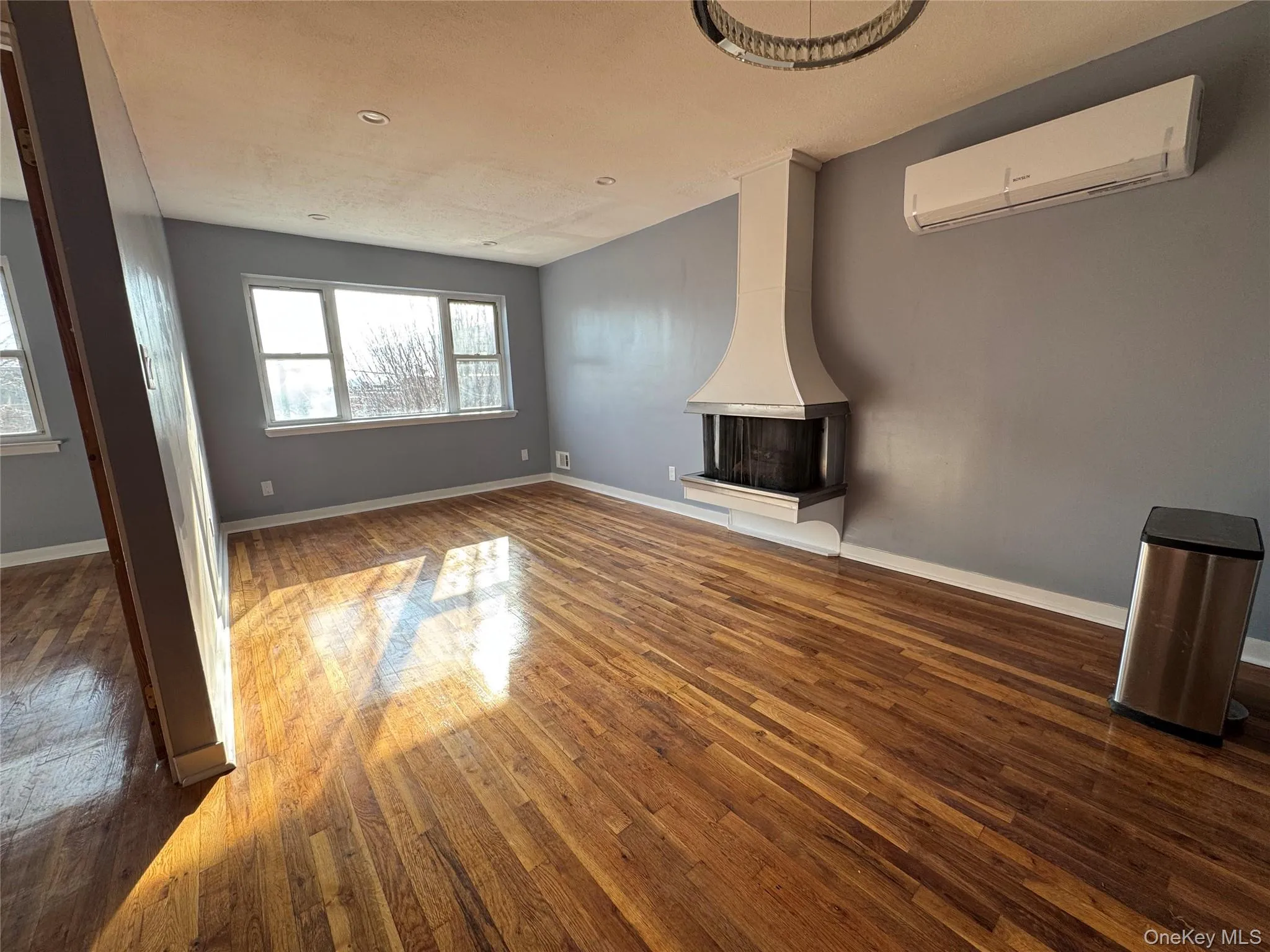 Unfurnished living room featuring a wall mounted AC and dark wood-style floors Unfurnished living room featuring a wall mounted AC and dark wood-style floors