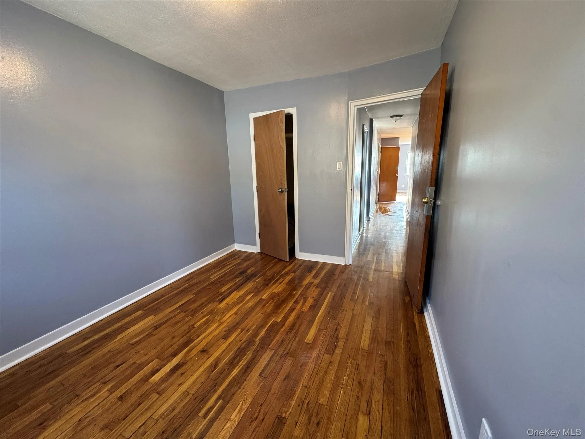 Unfurnished bedroom featuring dark wood-type flooring, a textured ceiling, and a closet Unfurnished bedroom featuring dark wood-type flooring, a textured ceiling, and a closet