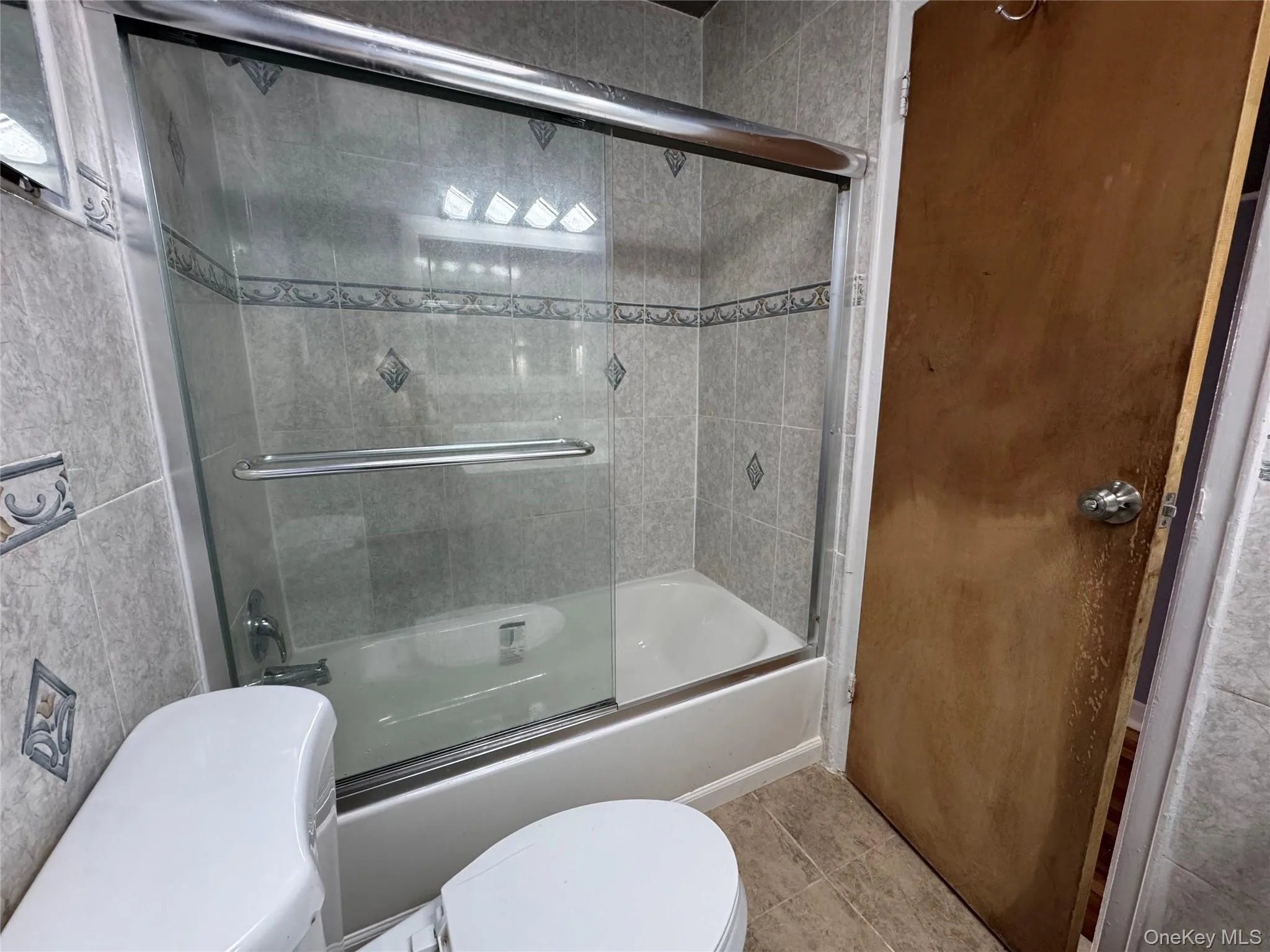 Full bath with bath / shower combo with glass door and light tile patterned flooring Full bath with bath / shower combo with glass door and light tile patterned flooring