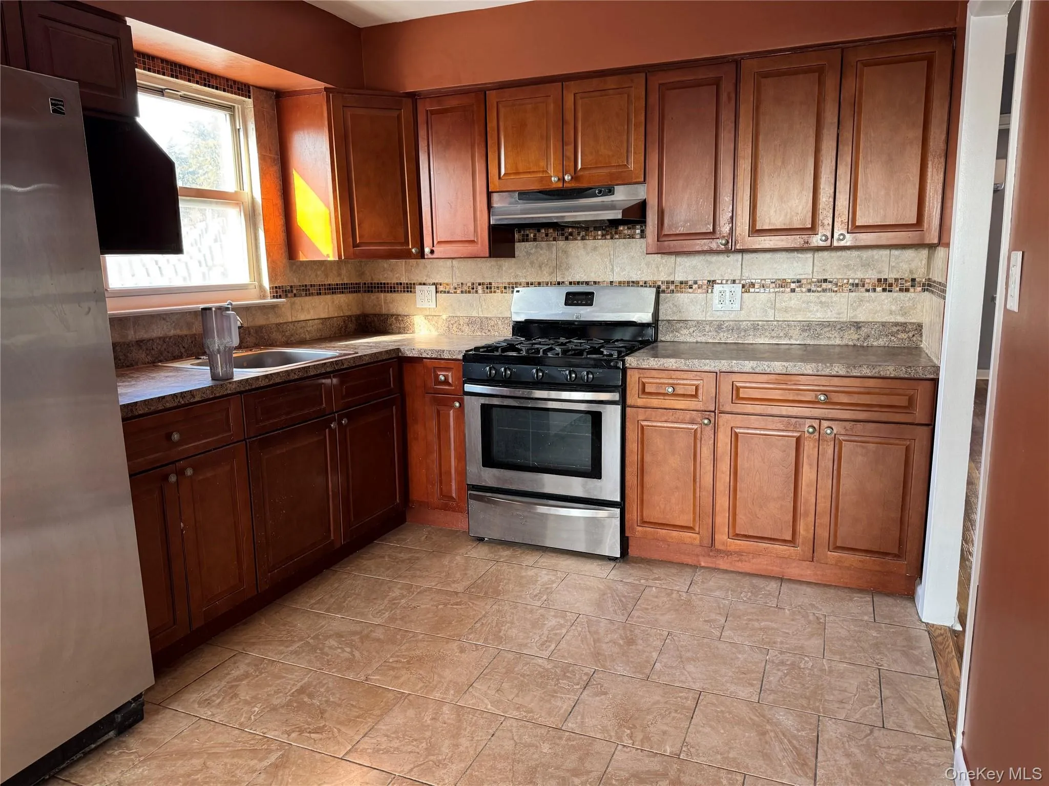 Kitchen with appliances with stainless steel finishes, under cabinet range hood, brown cabinets, and tasteful backsplash Kitchen with appliances with stainless steel finishes, under cabinet range hood, brown cabinets, and tasteful backsplash