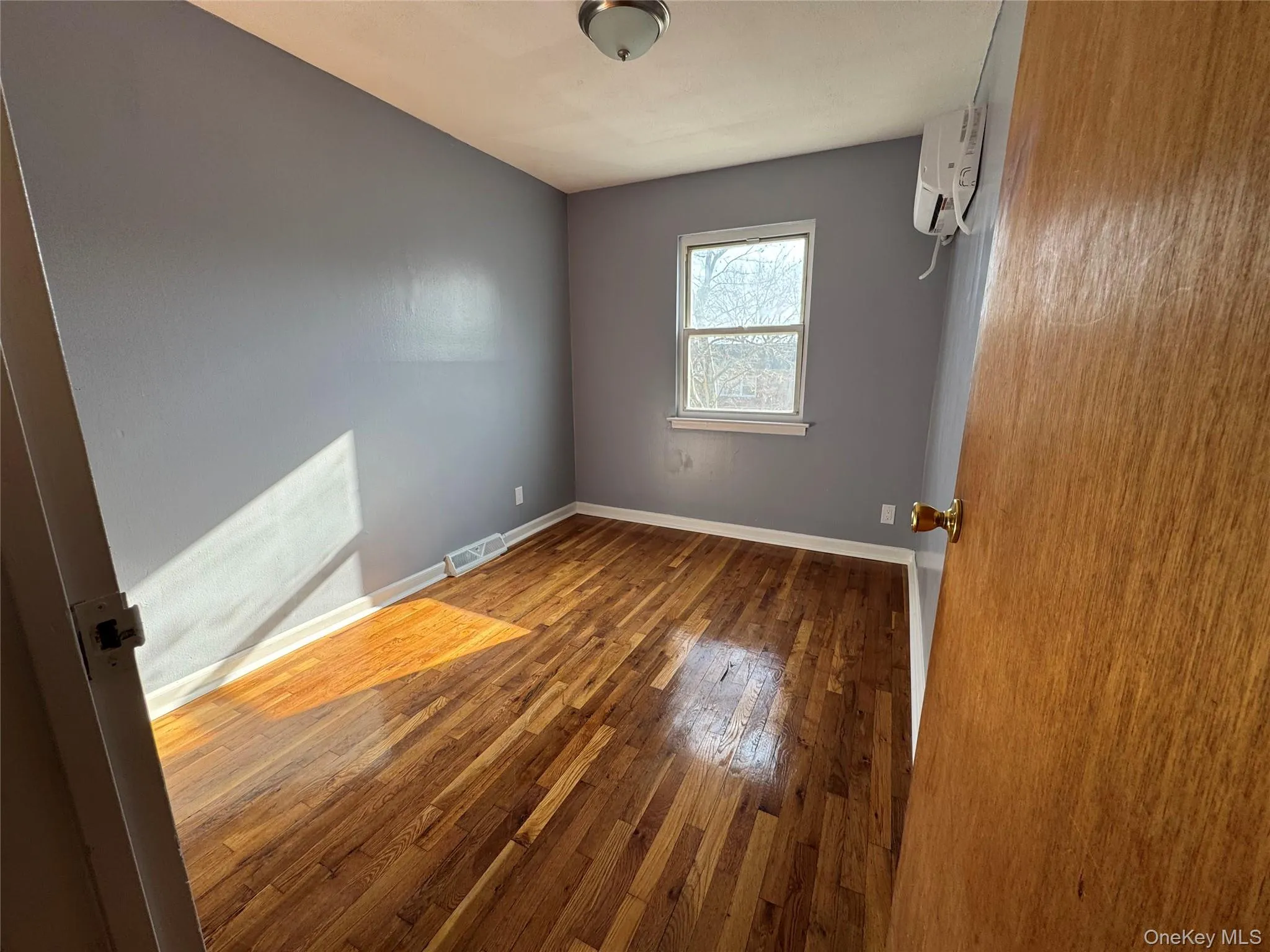 Unfurnished room featuring hardwood / wood-style floors and a wall mounted air conditioner Unfurnished room featuring hardwood / wood-style floors and a wall mounted air conditioner